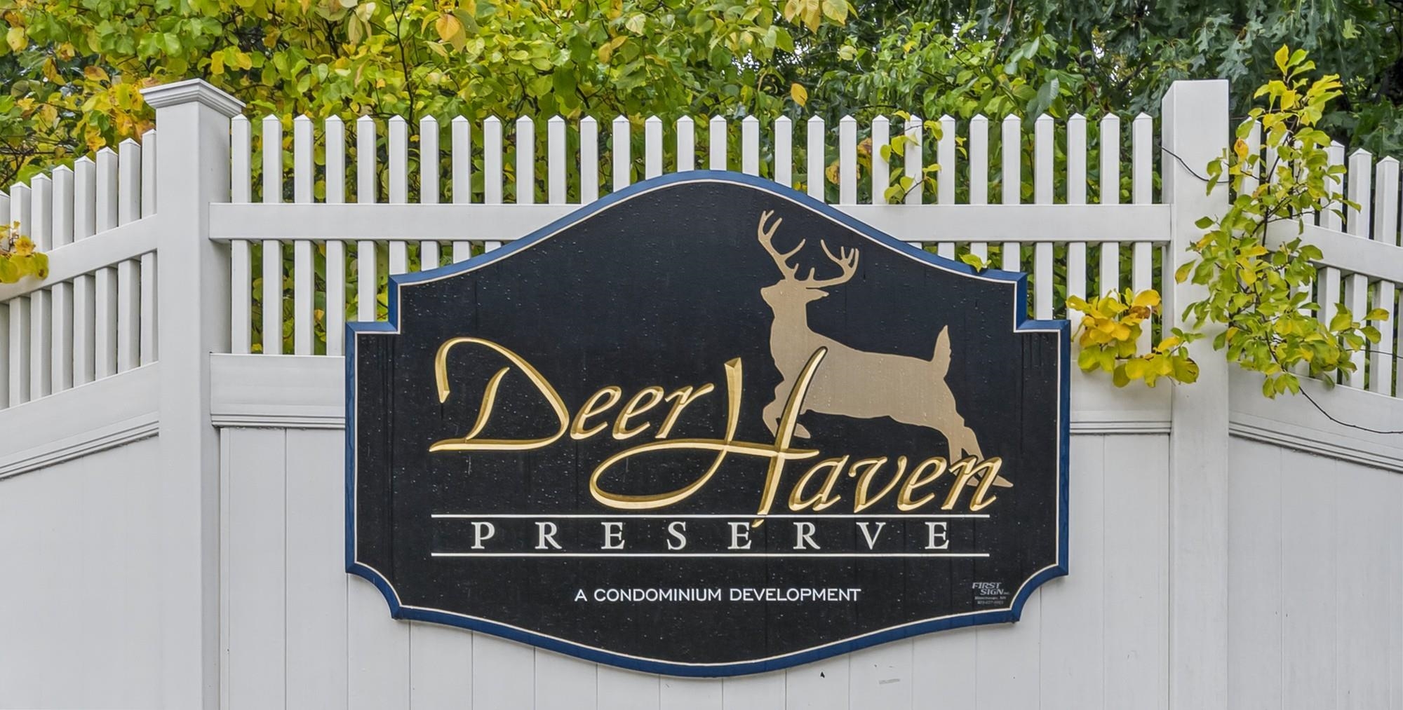 Deer Haven Preserve condominium entrance sign on a white fence amid autumn foliage.