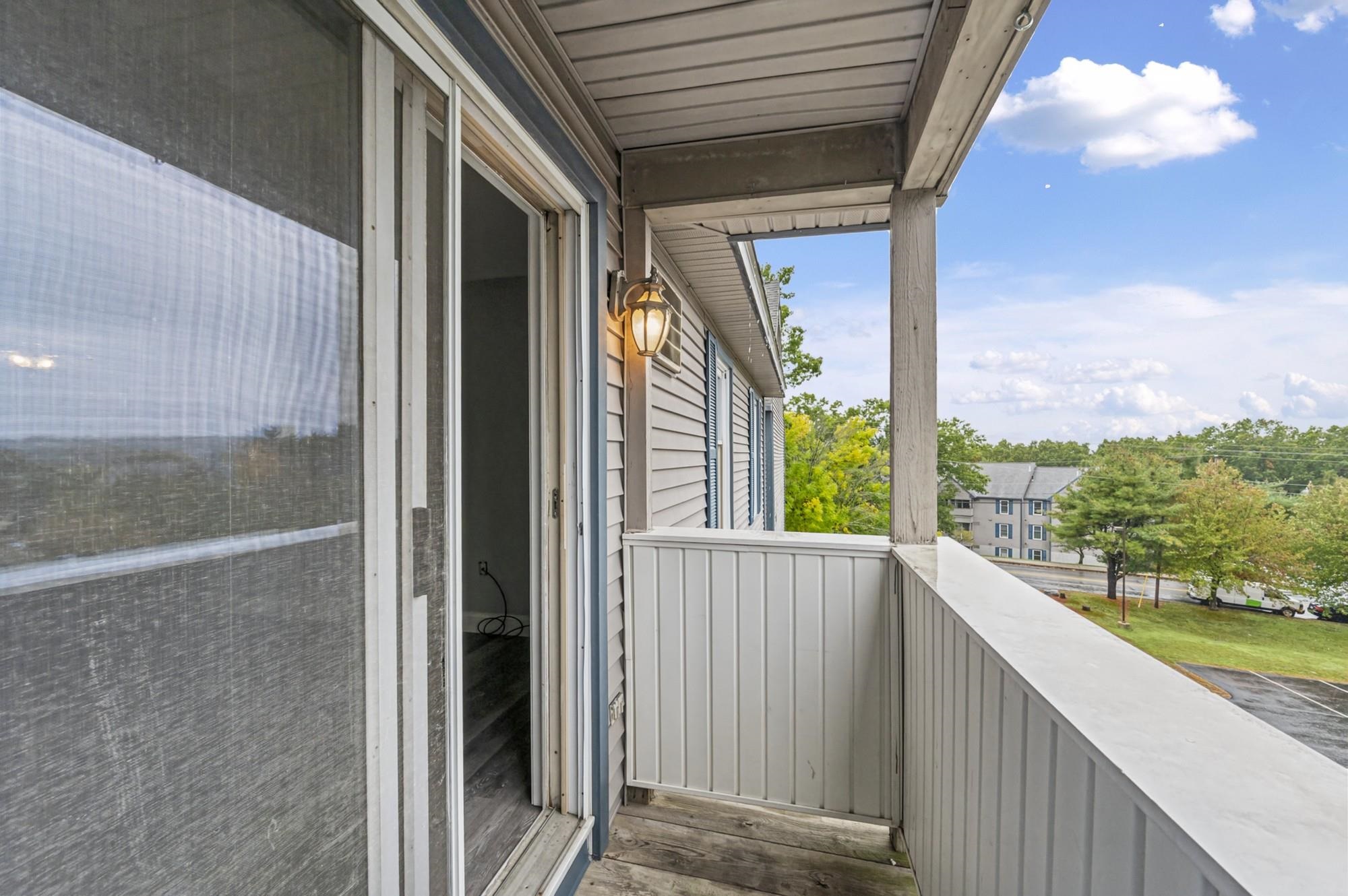 Covered balcony with white railing overlooking trees and nearby buildings.