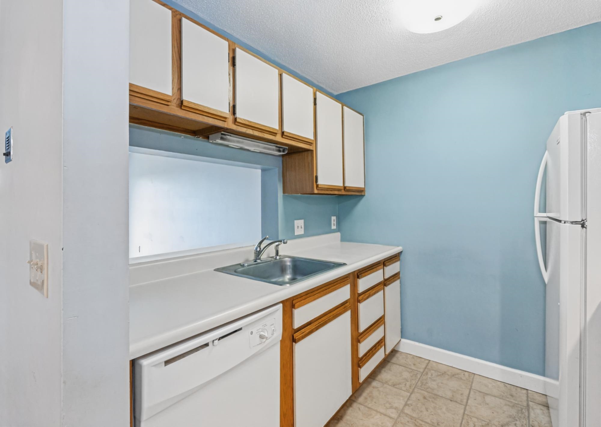 Kitchen with blue walls, wood-trimmed cabinets, white counters, and a stainless-steel sink.