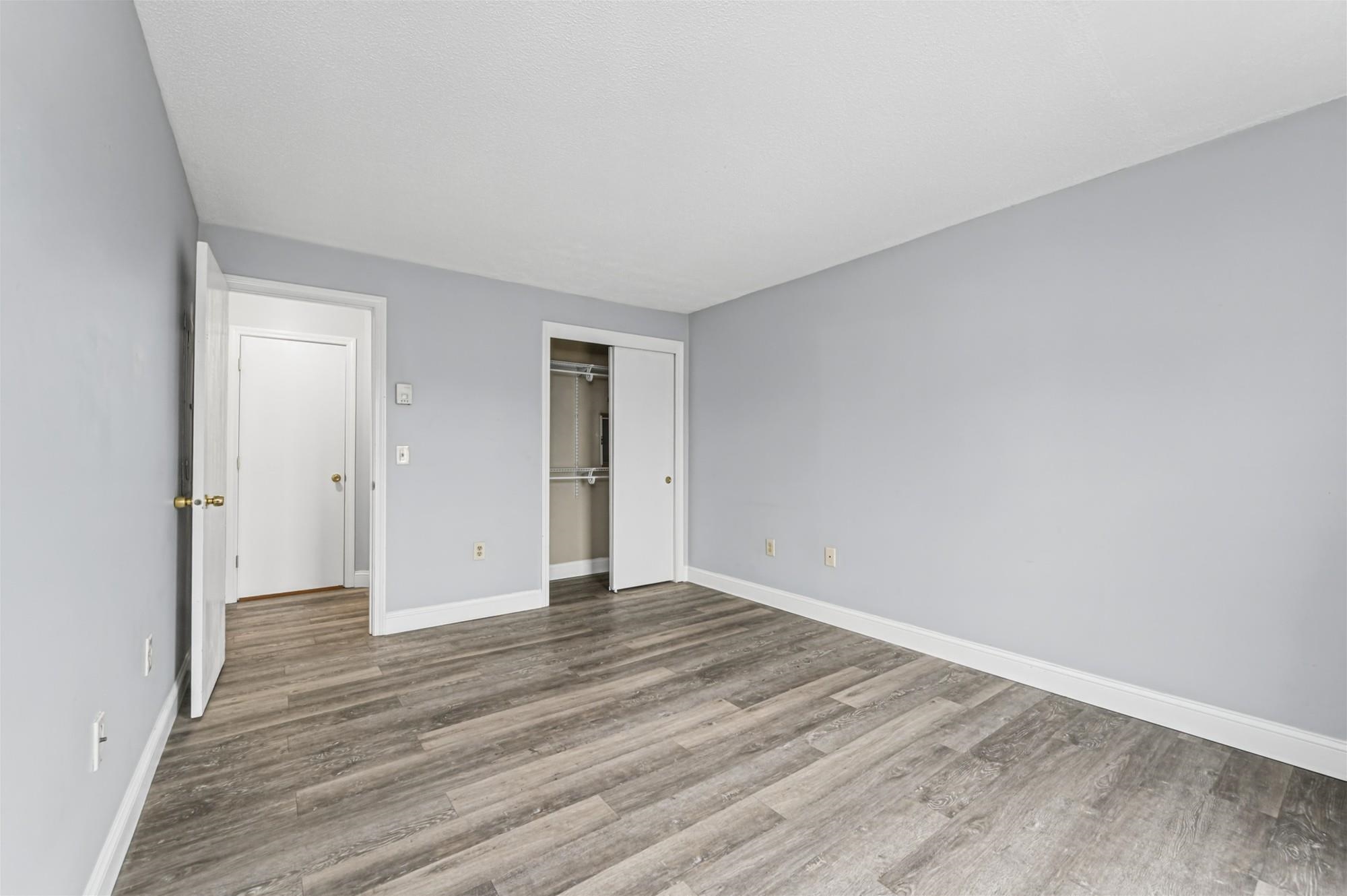 Empty bedroom with gray-brown plank flooring and an open closet.