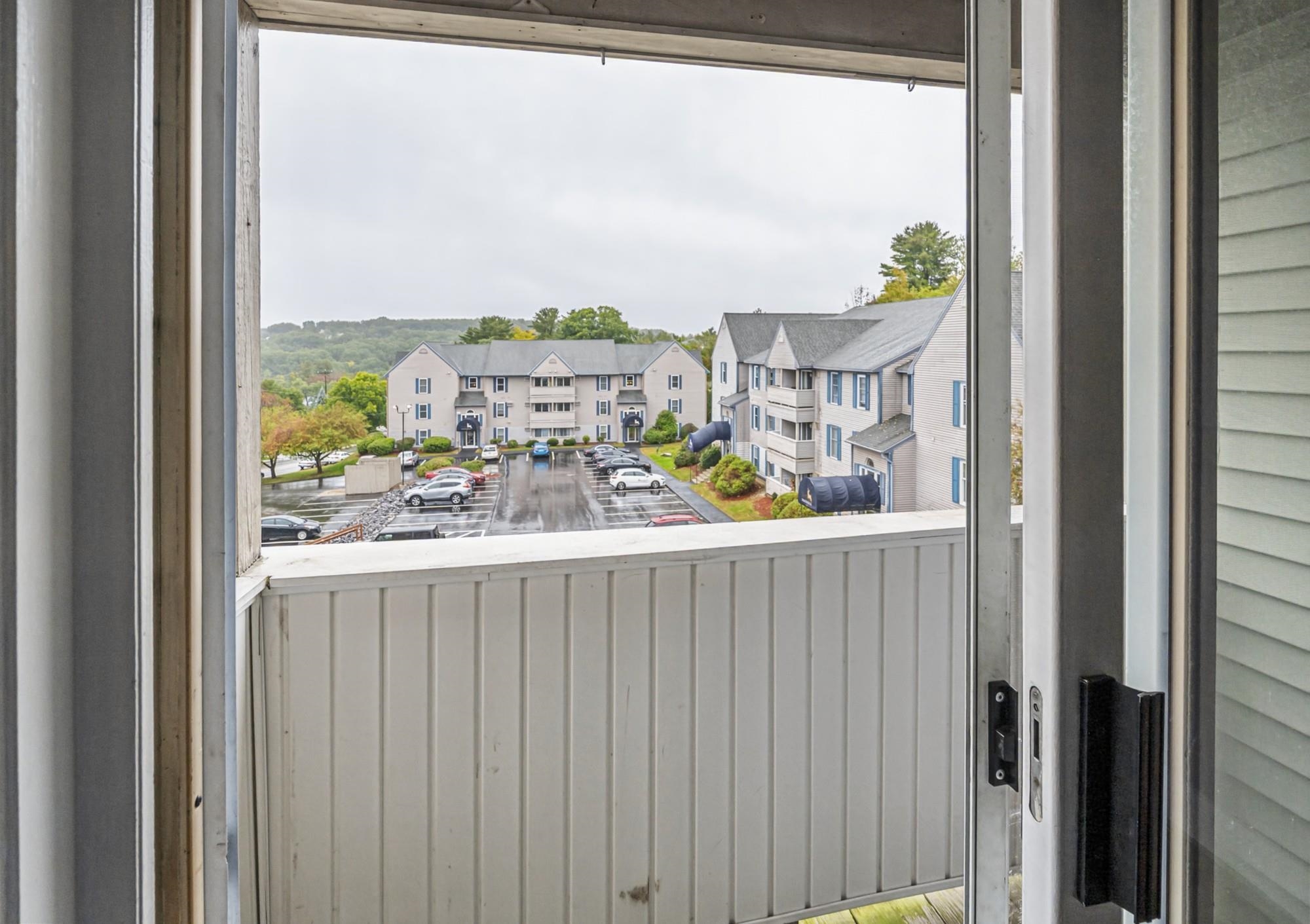 Apartment balcony overlooking neighboring buildings and a wet parking lot.