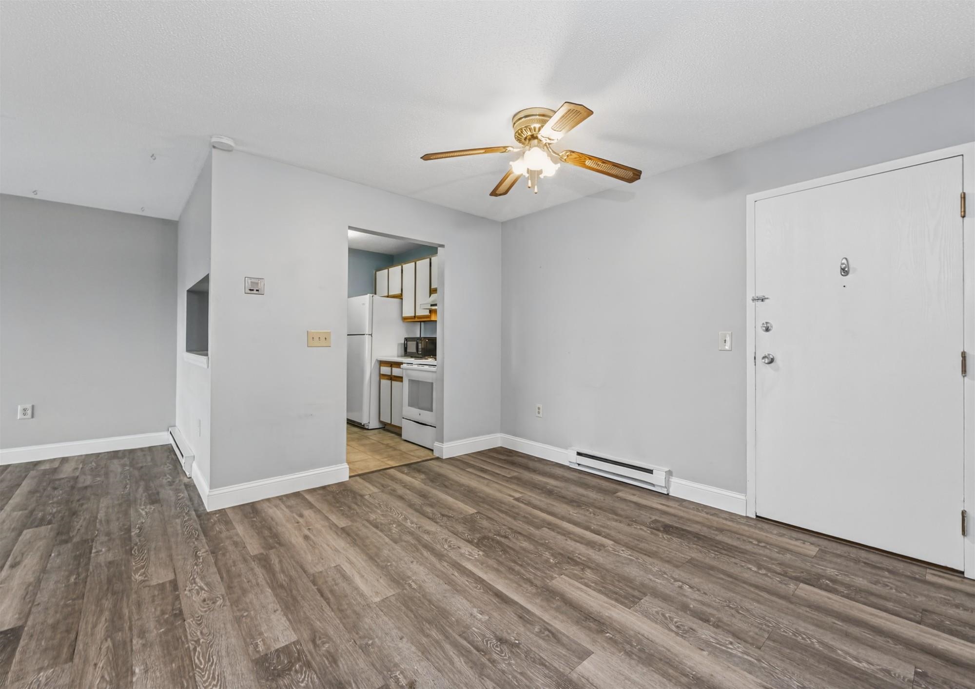 Empty apartment living area with wood-look floors, ceiling fan, and kitchen doorway.