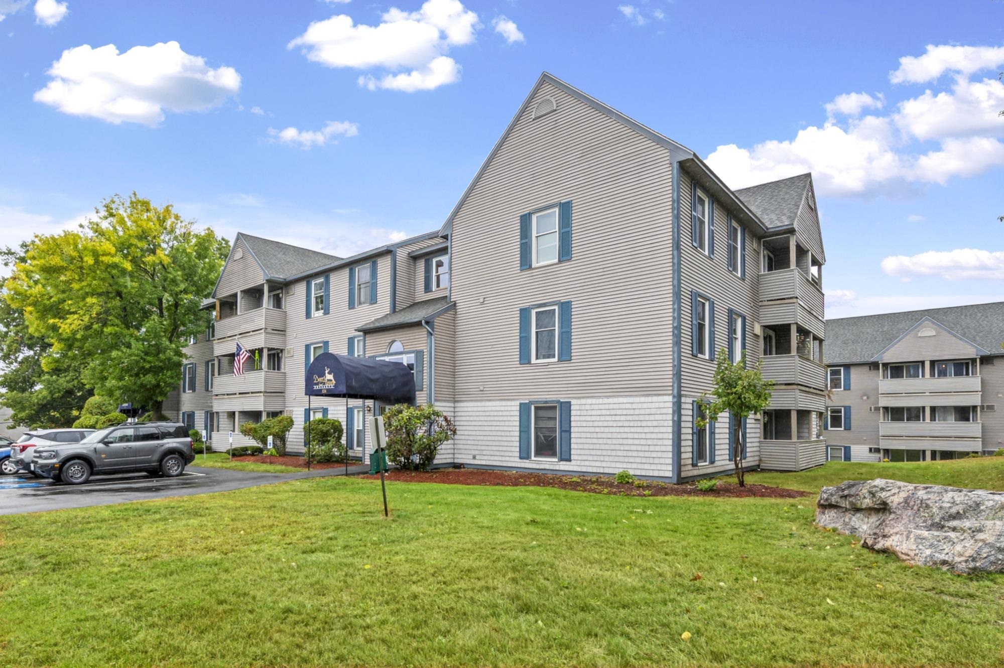Multi-unit building with gray siding, blue shutters, balconies, and a covered entrance.