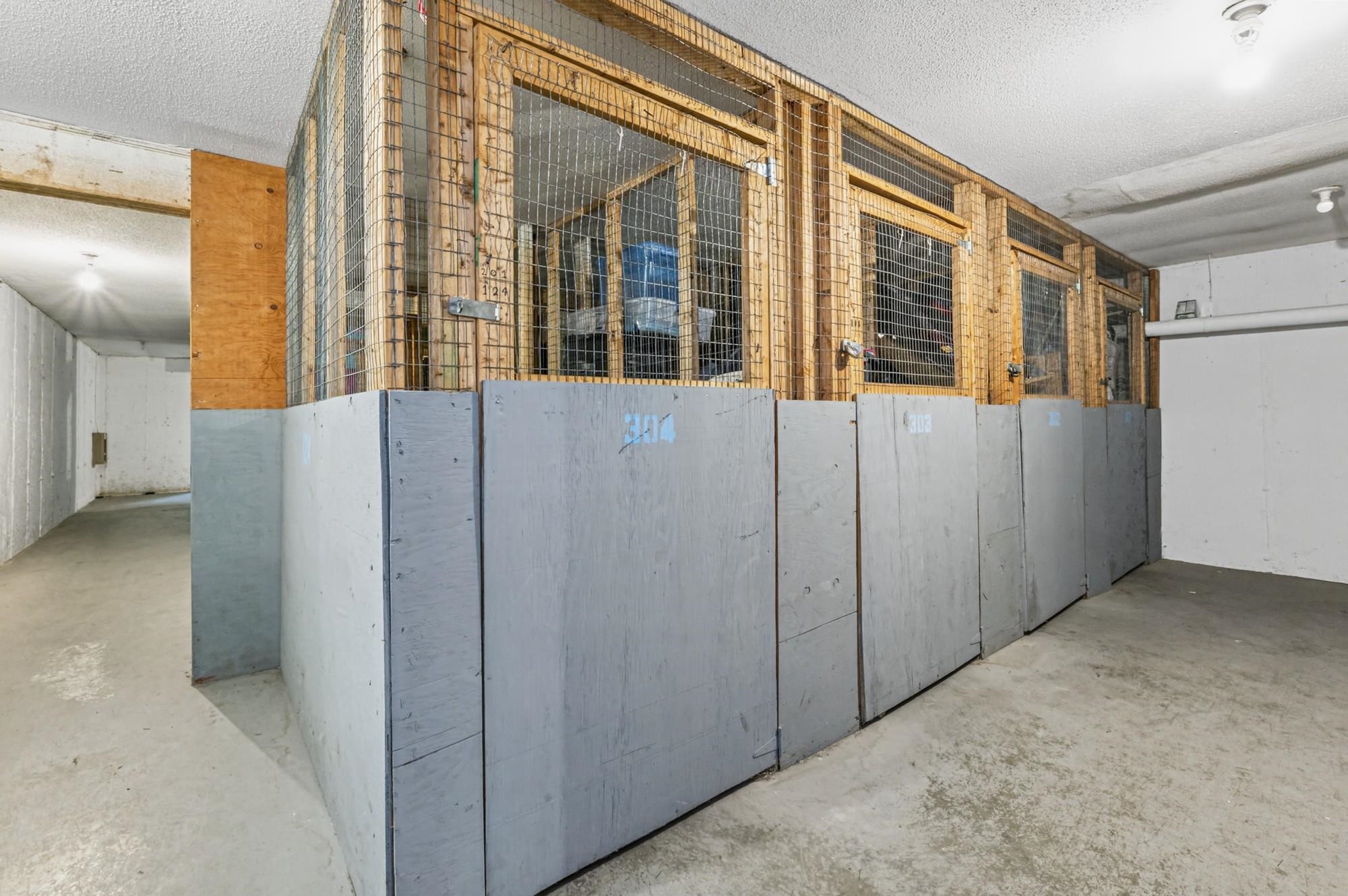Indoor storage area with wooden wire-mesh cages and gray lower panels along a concrete floor.