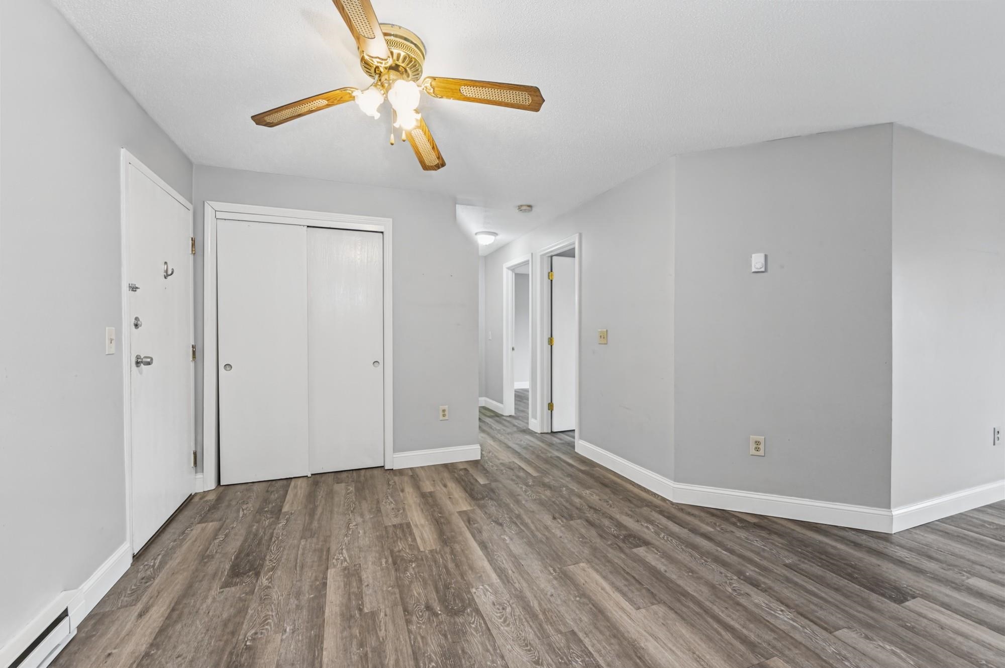 Unfurnished condo room with gray walls, wood-look floors, a ceiling fan, and a hallway.