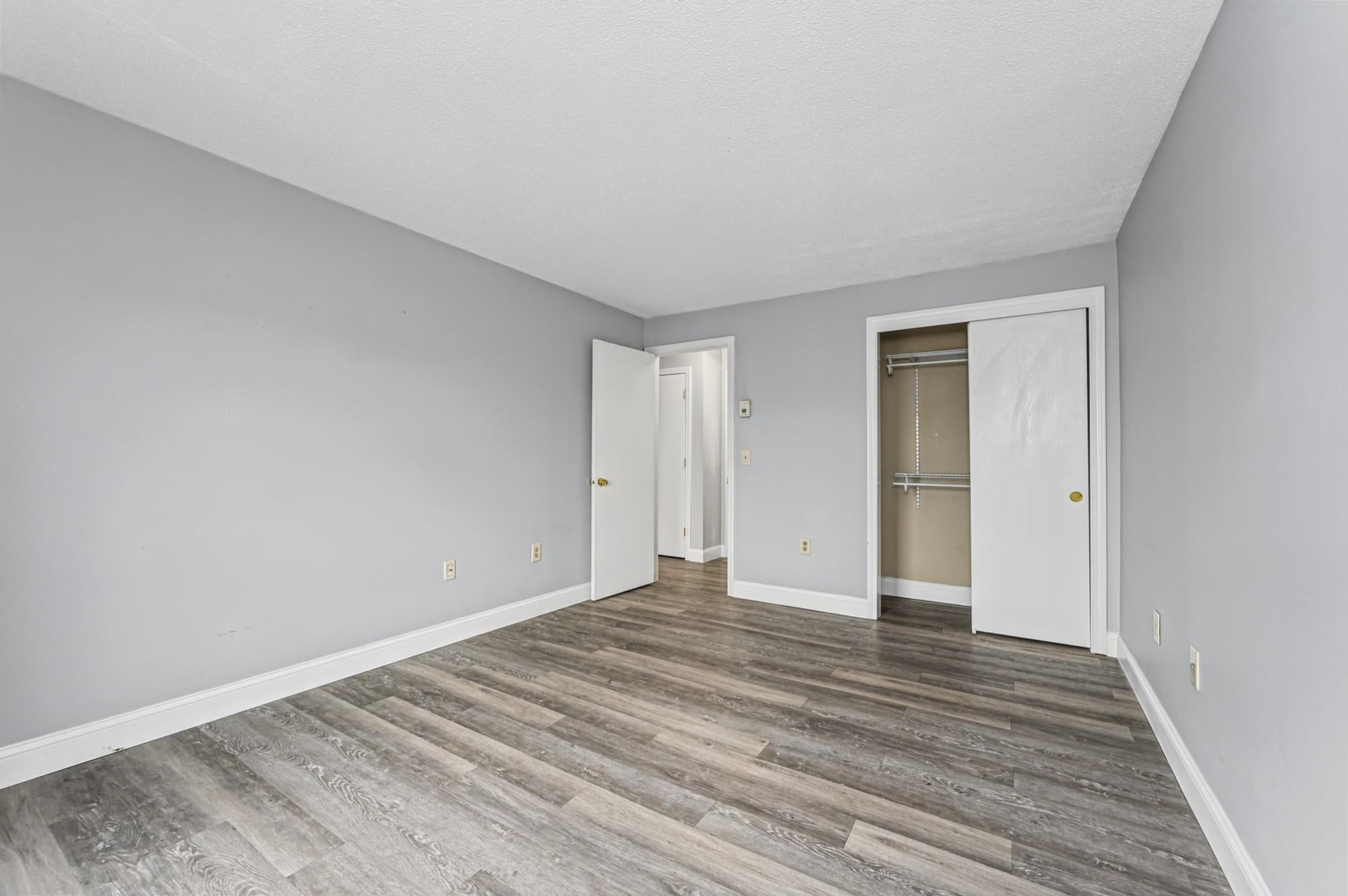 Vacant bedroom with gray walls, wood-look flooring, and an open closet with wire shelving.