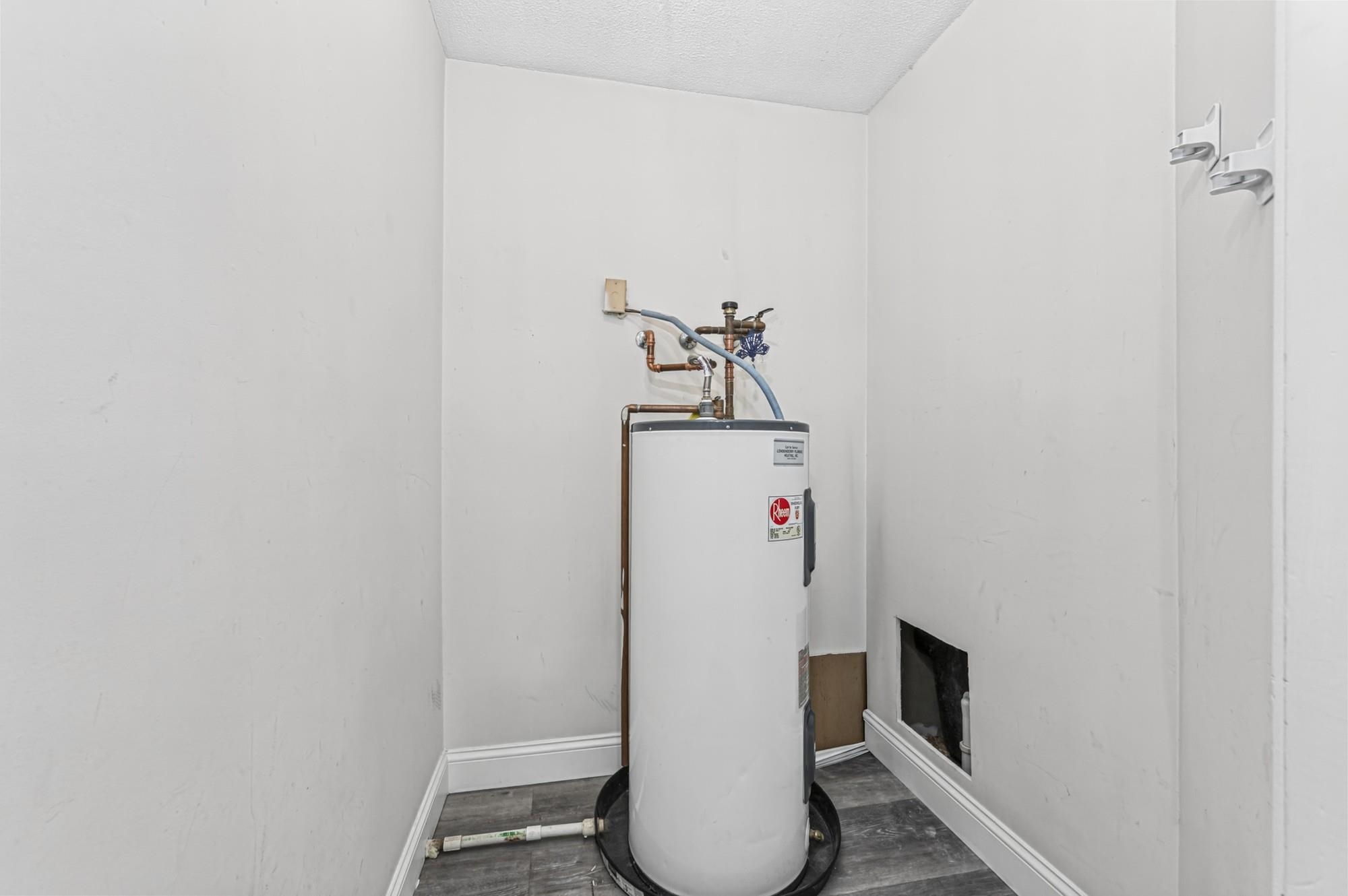Utility closet with a tall water heater, exposed plumbing, and gray flooring.