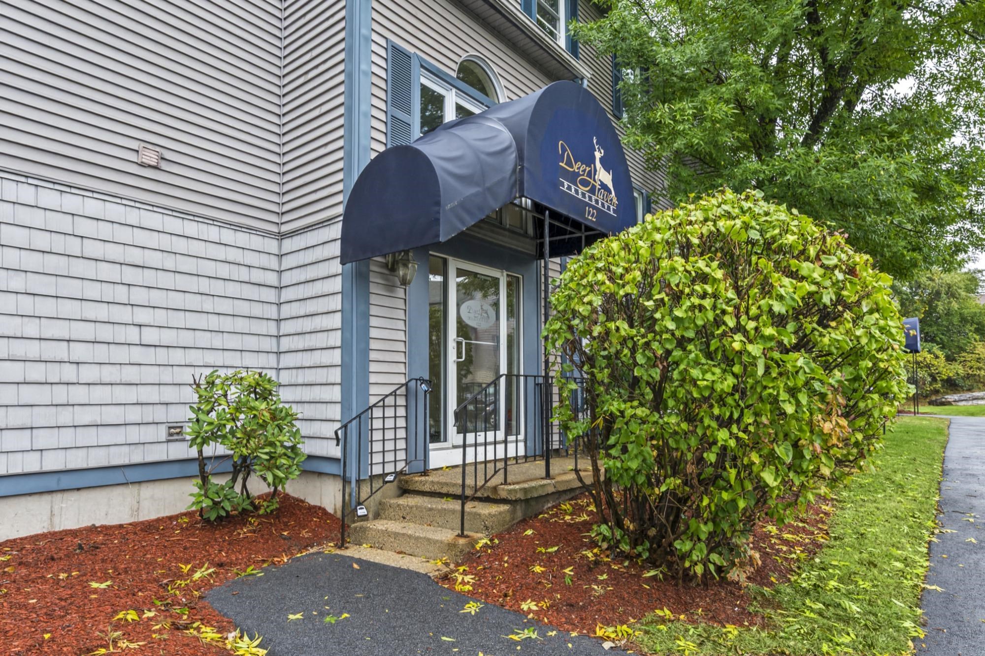 Building entrance with a navy Deer... Preserve awning, concrete steps, and landscaped shrubs.