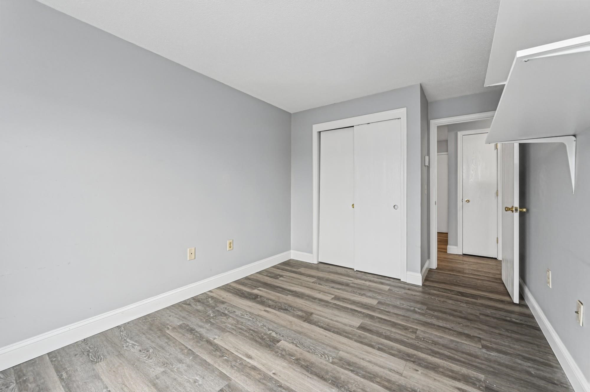 Unfurnished room with gray-brown plank flooring, a white sliding closet, and an open doorway to the hall.