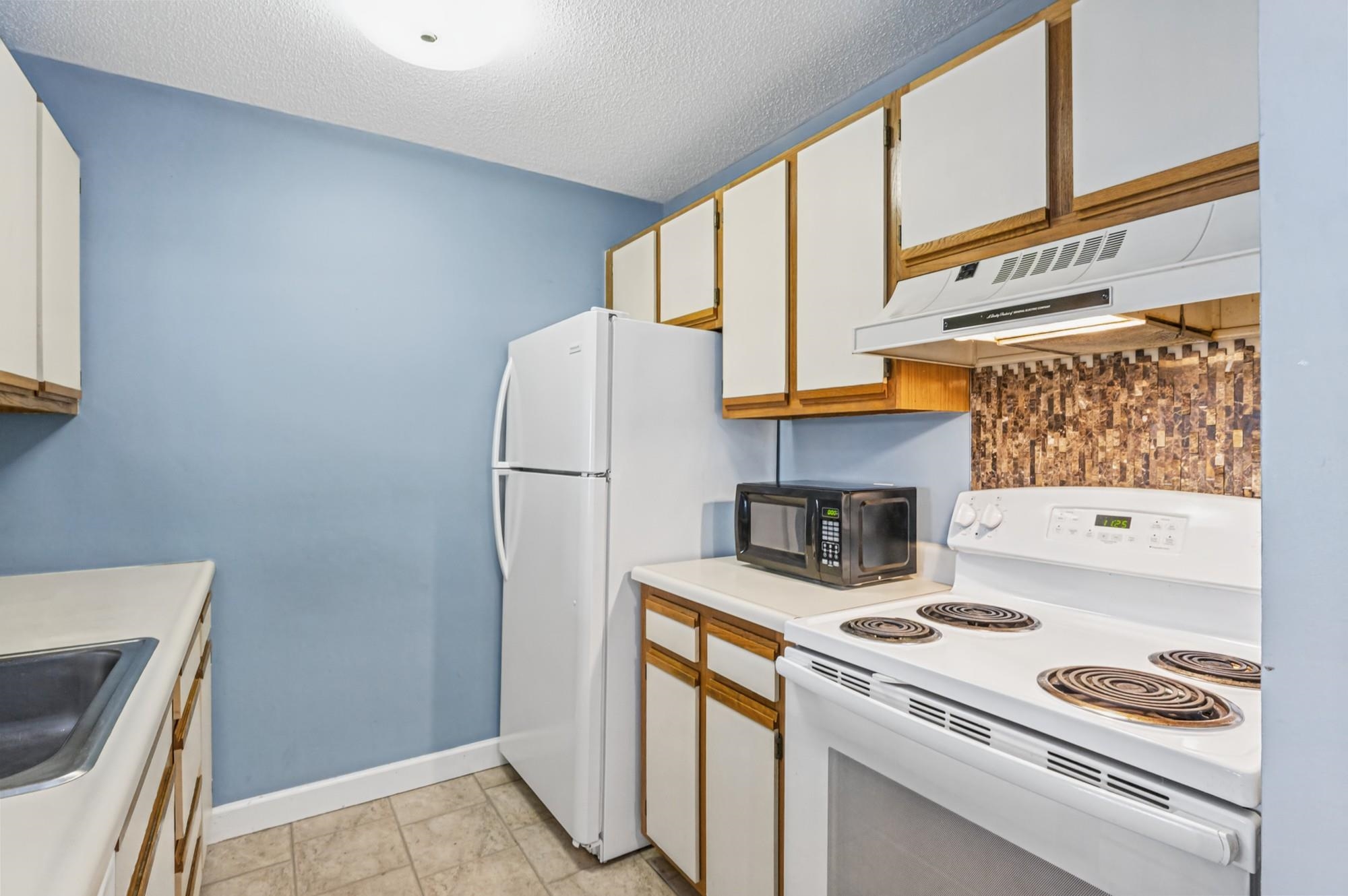 Kitchen with white appliances, wood-trimmed cabinets, and a patterned tile backsplash.