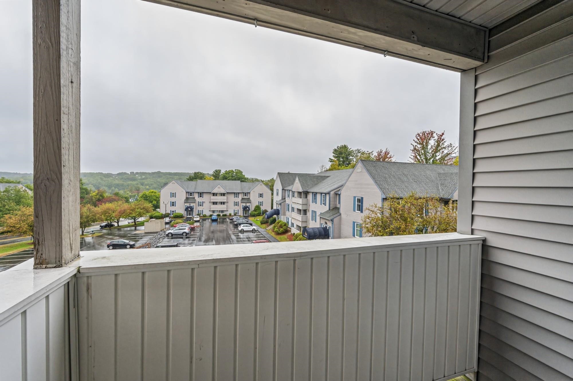 Covered balcony overlooking neighboring buildings, a parking lot, and autumn-colored wooded hills.