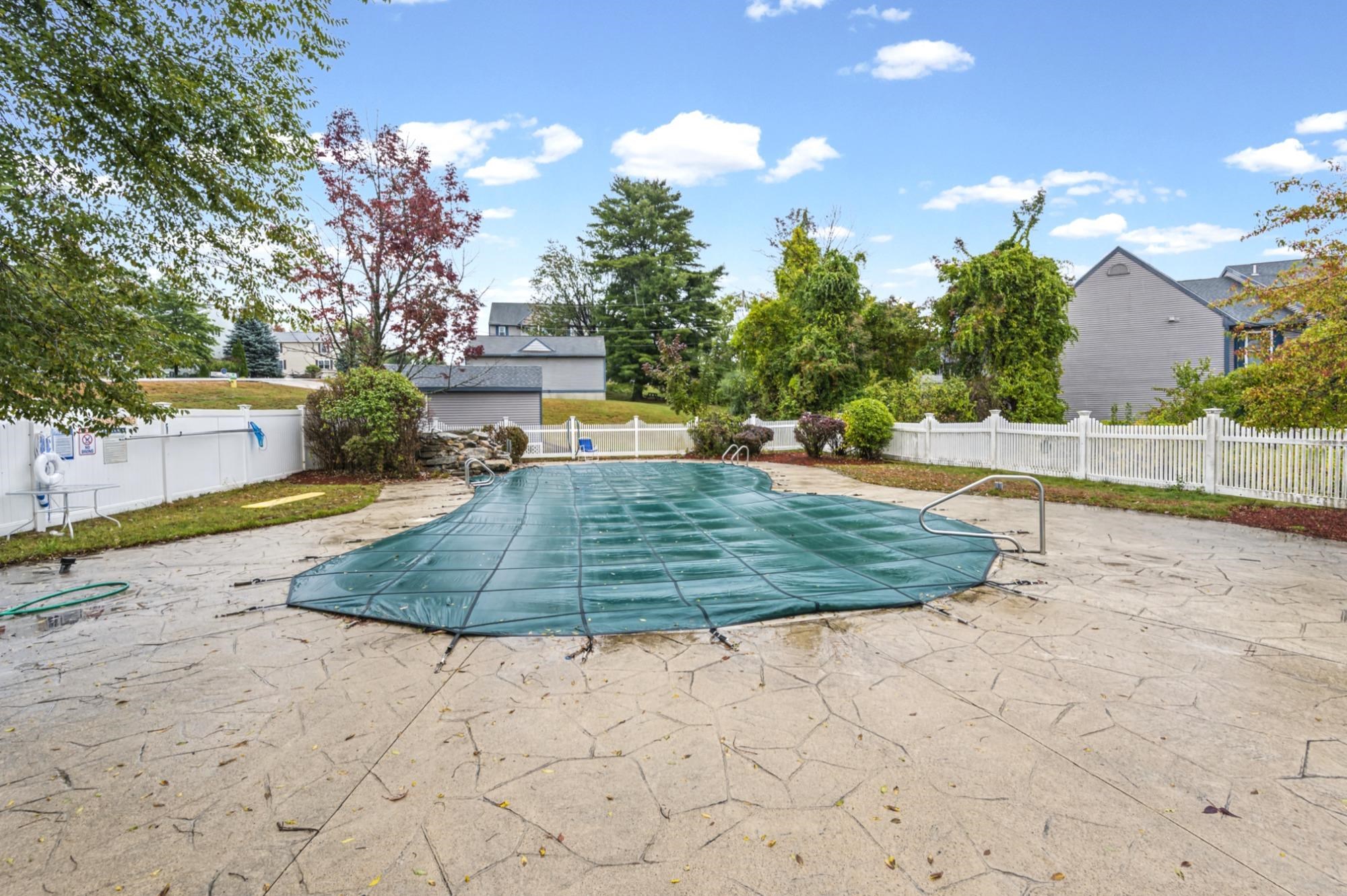 Covered outdoor swimming pool with a teal cover, stone patio, and white fence.
