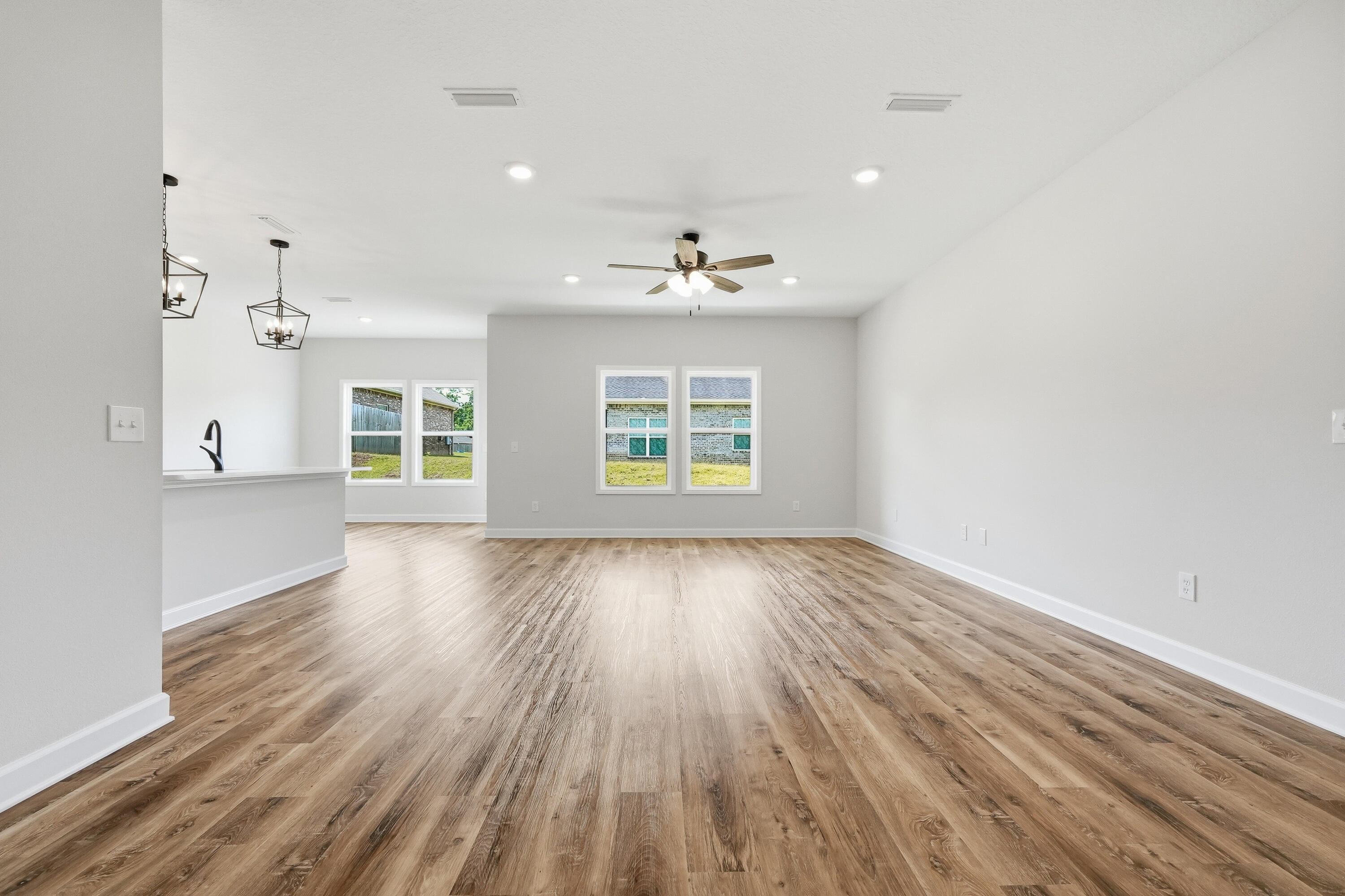 Empty living and dining area with wood-look flooring, a ceiling fan, and a kitchen peninsula.
