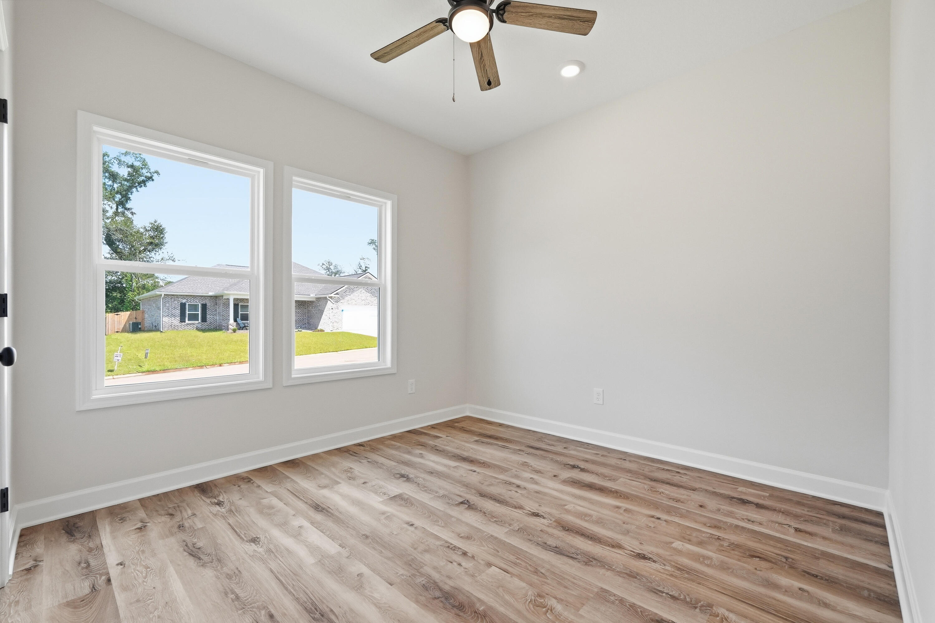 Vacant room with wood-look flooring, two windows, and a wood-blade ceiling fan.