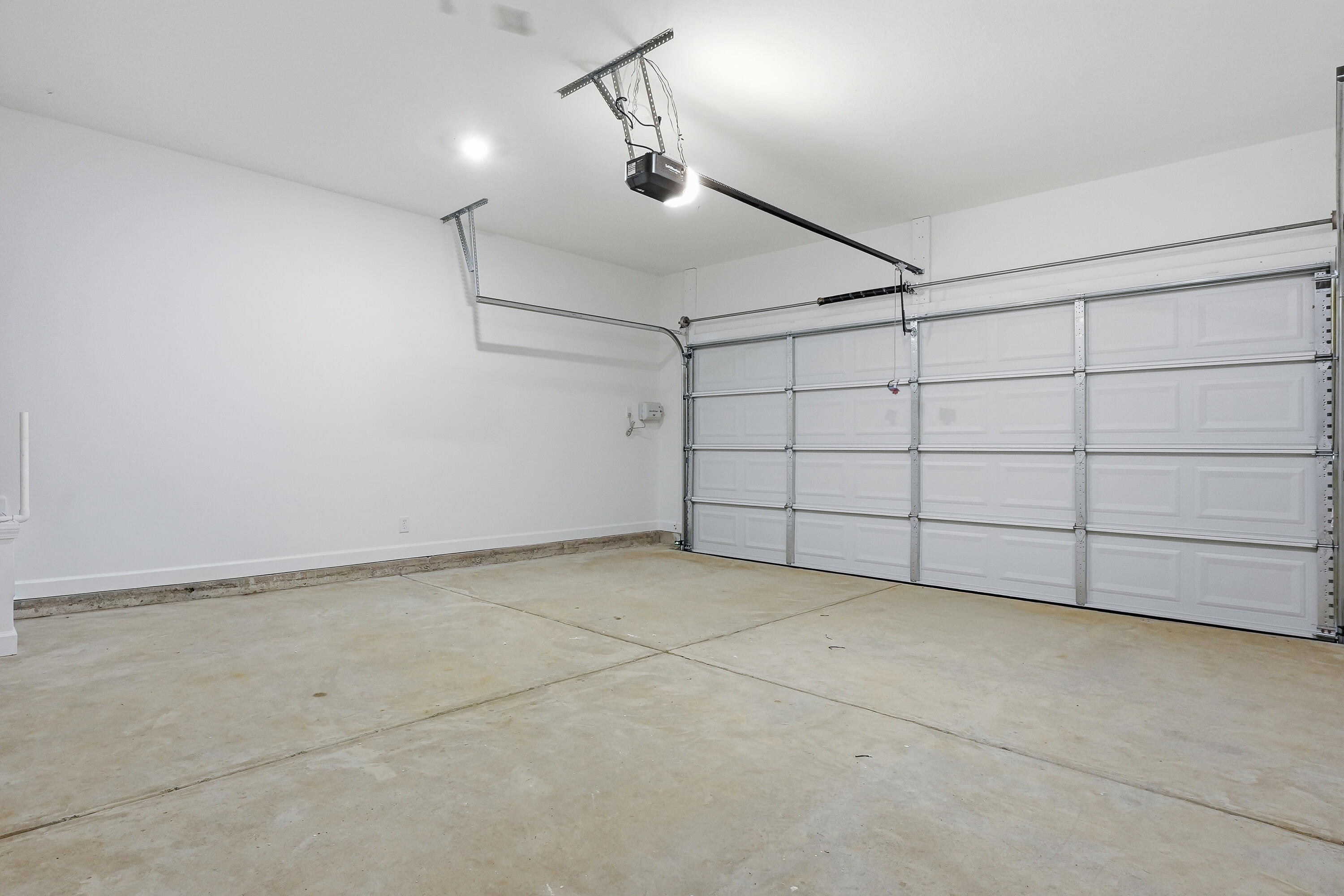 Empty garage with a concrete floor, white walls, and a closed sectional door.