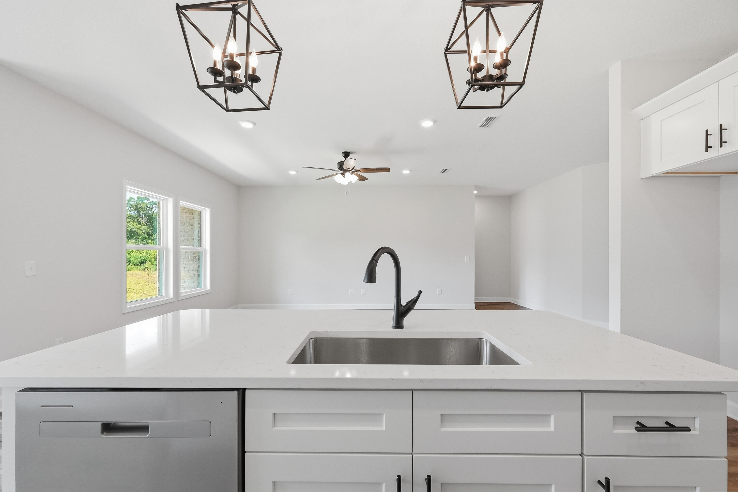 Vacant kitchen with a white island, stainless steel sink, dark faucet, and geometric pendant lights.