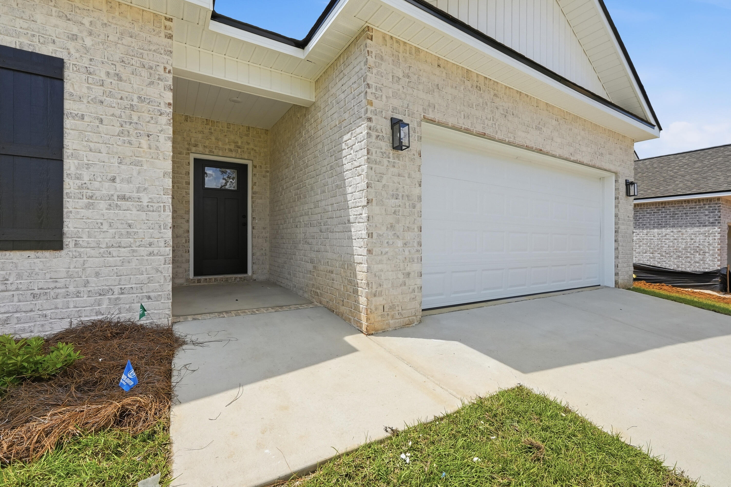 Light brick house exterior with a recessed black front door and white double garage door.