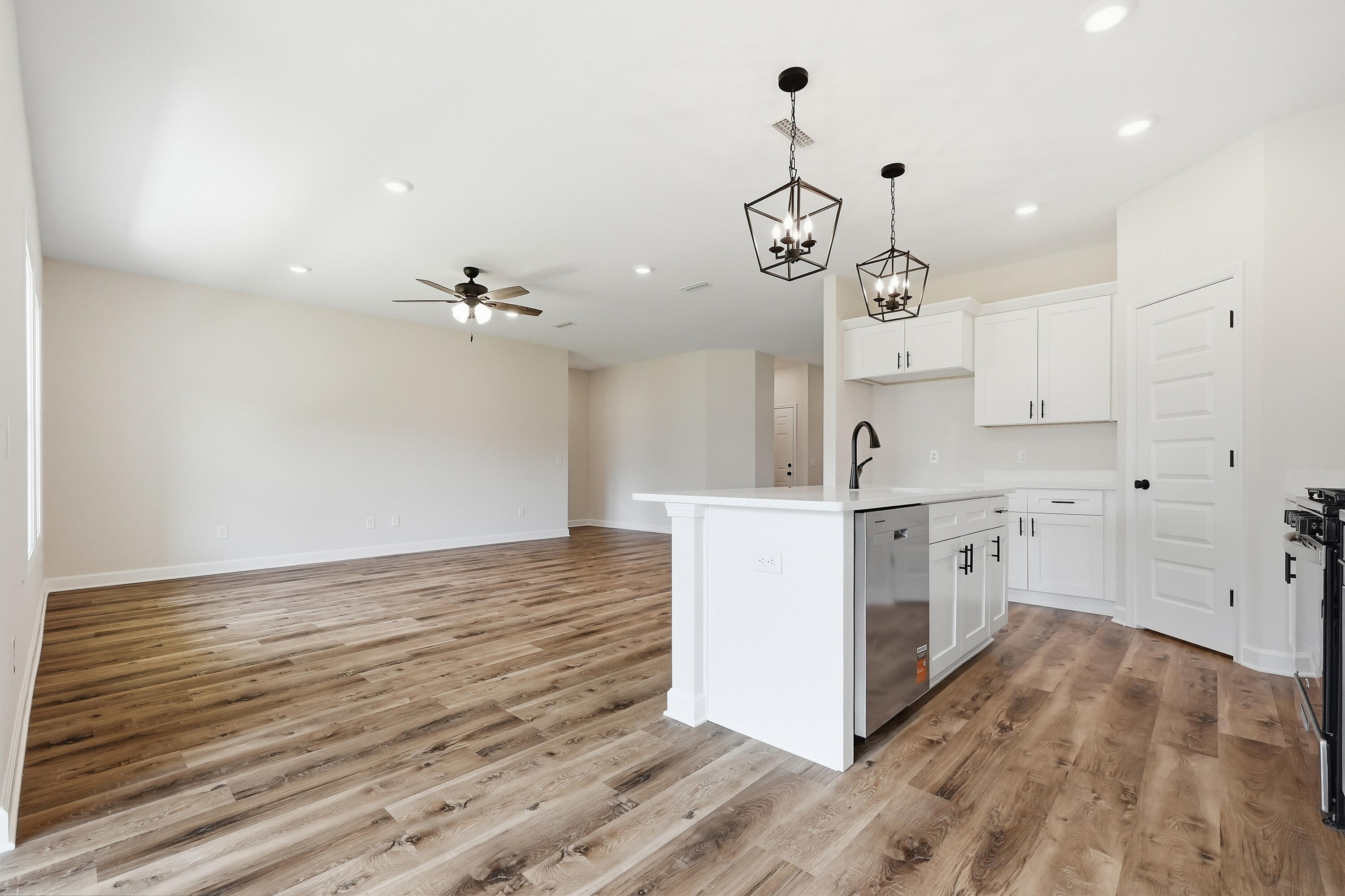 Open-plan kitchen with a large white island, stainless steel dishwasher, wood-look floors, and geometric pendant lights.