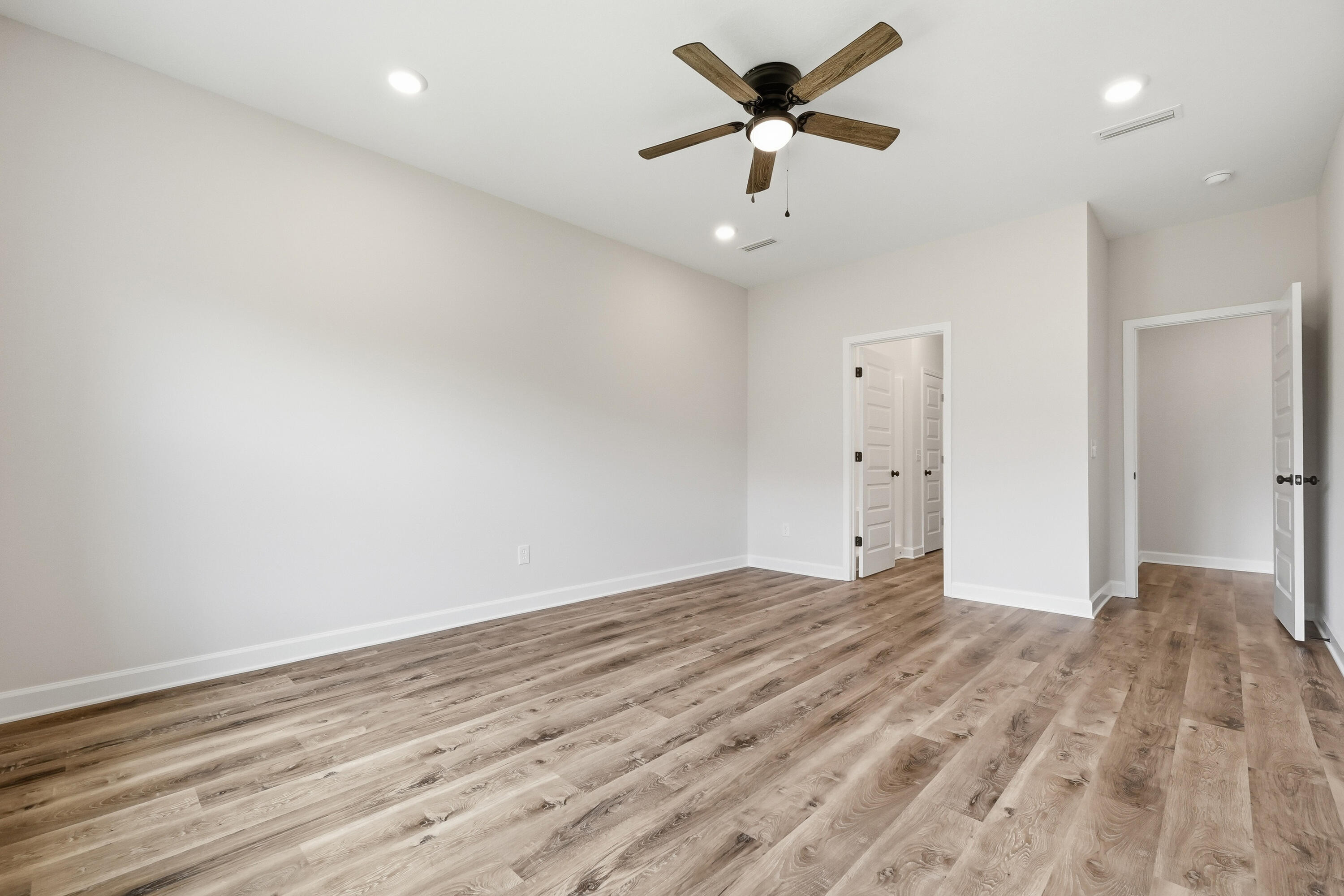 Empty bedroom with wood-look flooring, a ceiling fan, and two open doorways.