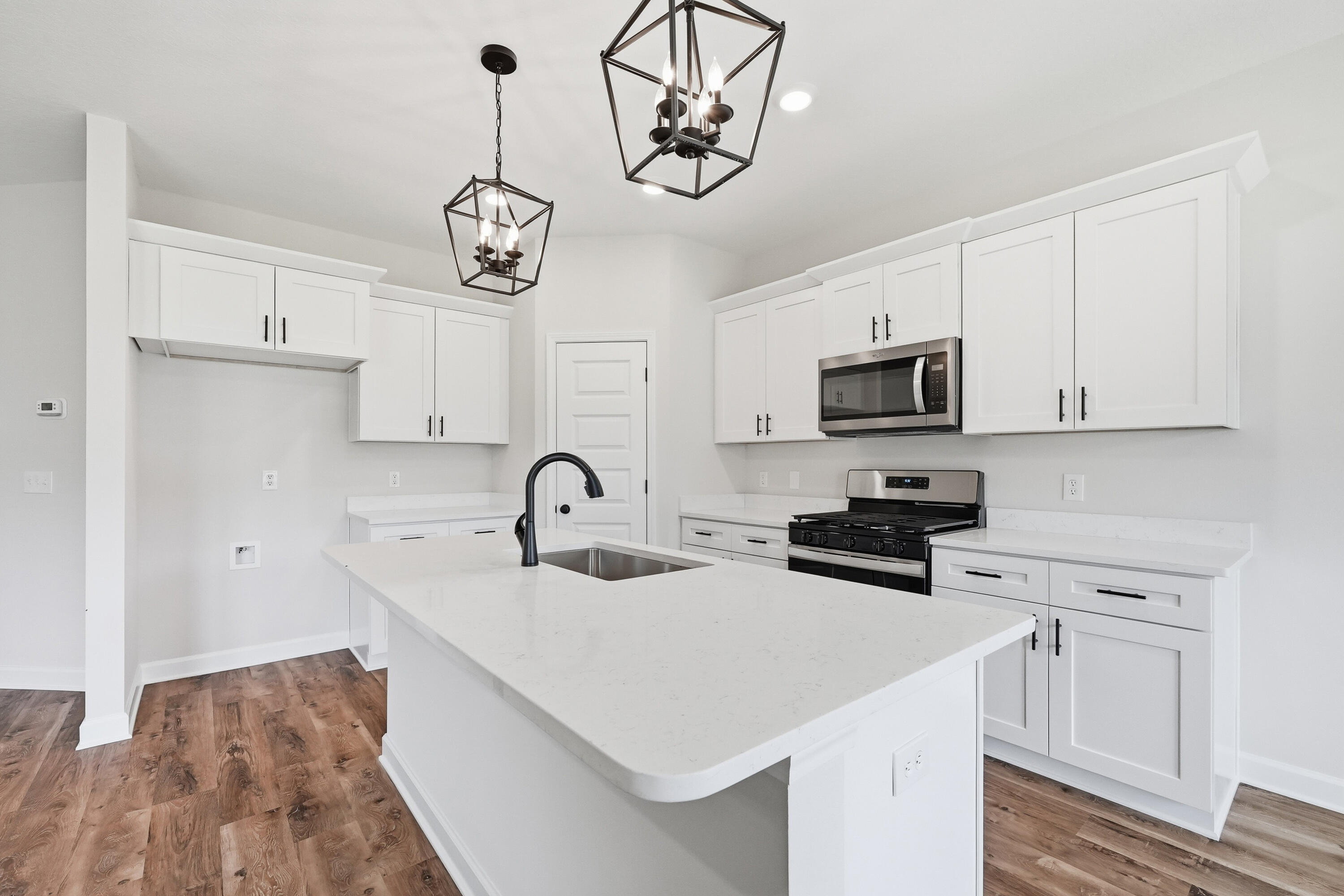 Bright kitchen with a large white island, black faucet, white cabinets, and stainless steel appliances.