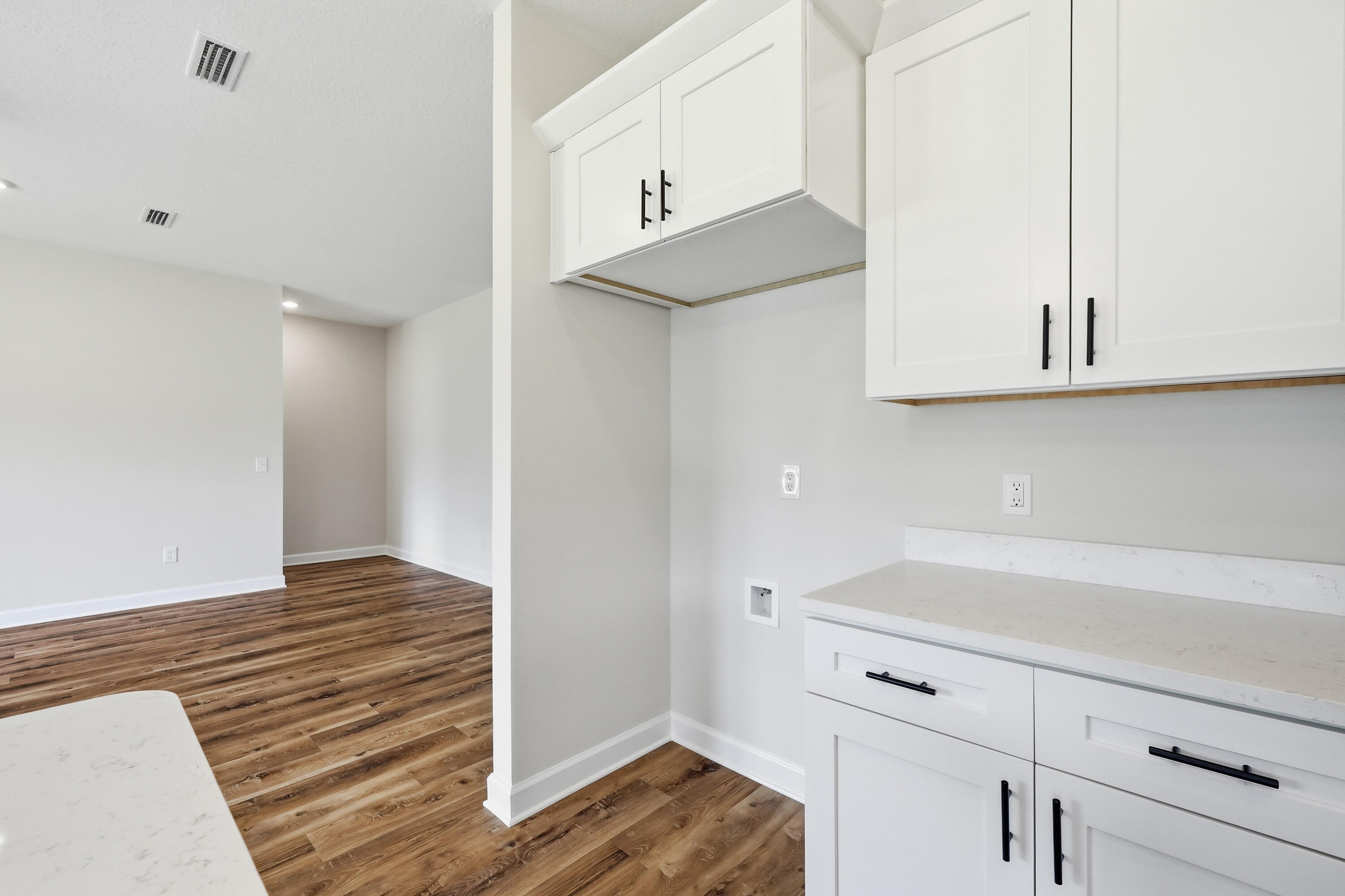 Kitchen with white cabinets, black hardware, white countertops, and warm wood-look flooring.