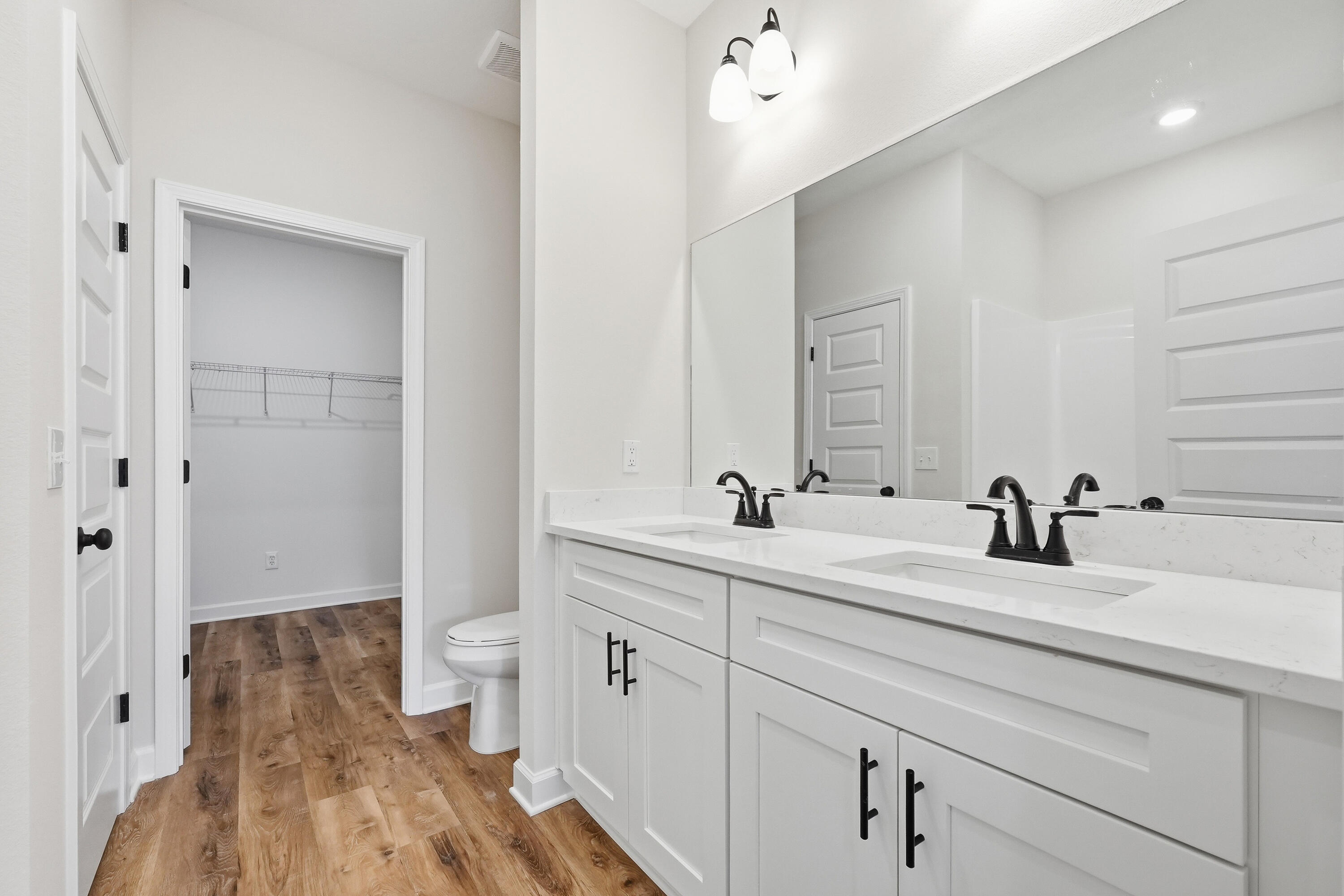 Bathroom with a white double vanity, black faucets, and wood-look flooring beside an open closet.