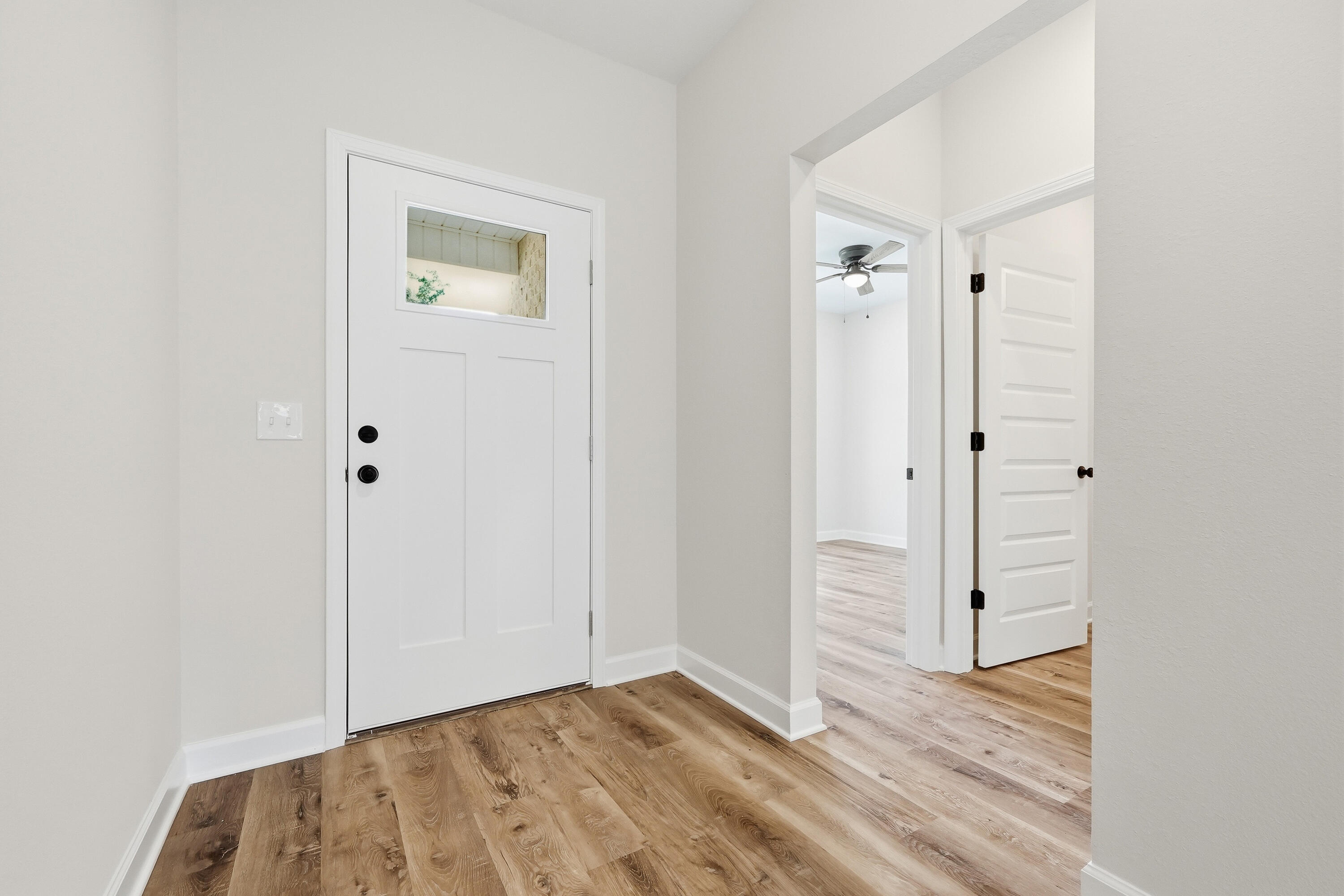 Vacant entryway with a white front door, warm wood-look floors, and open doorways to adjoining rooms.