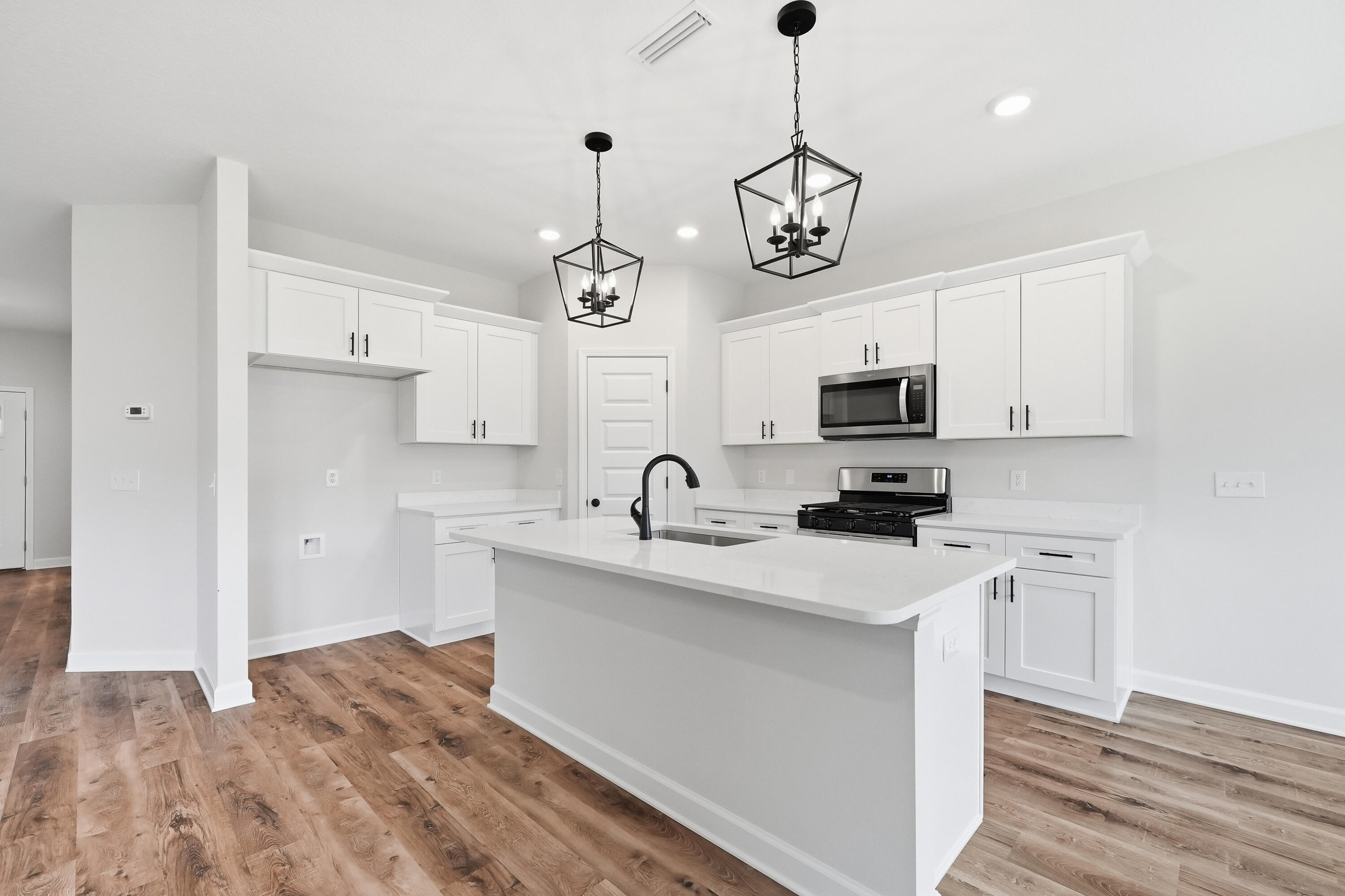 Kitchen with a large white island, stainless steel appliances, and black lantern pendant lights.