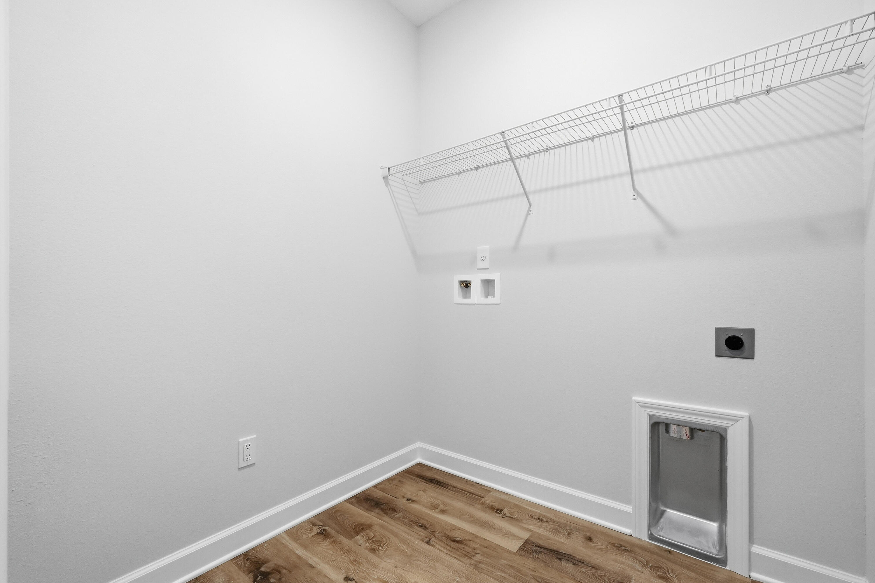 Empty laundry room with a wire shelf, washer hookups, wood-look flooring, and a low pet door.