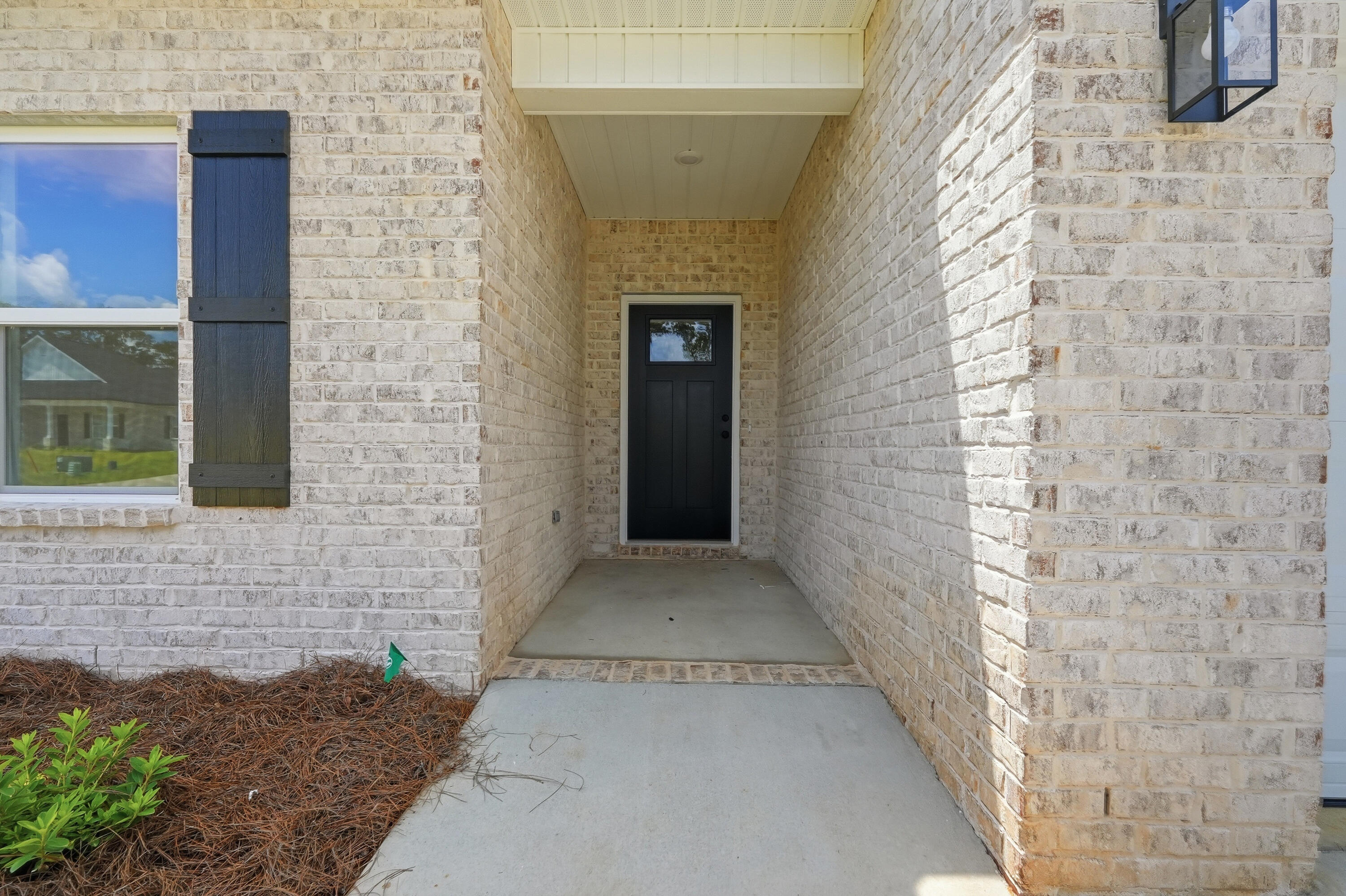 Covered brick entry with a black front door and window with dark shutters.