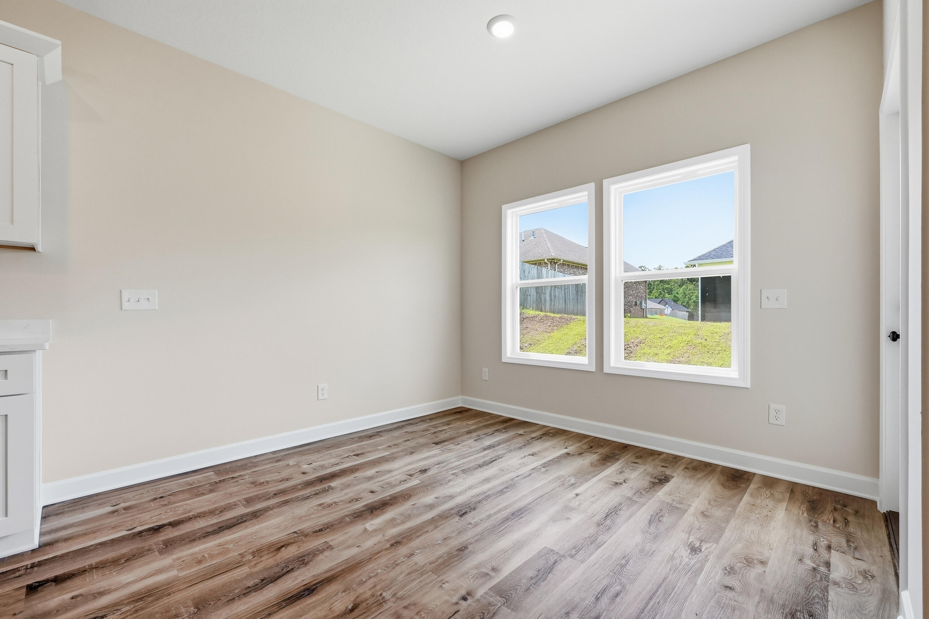 Empty room with two windows and wide-plank wood-look flooring.