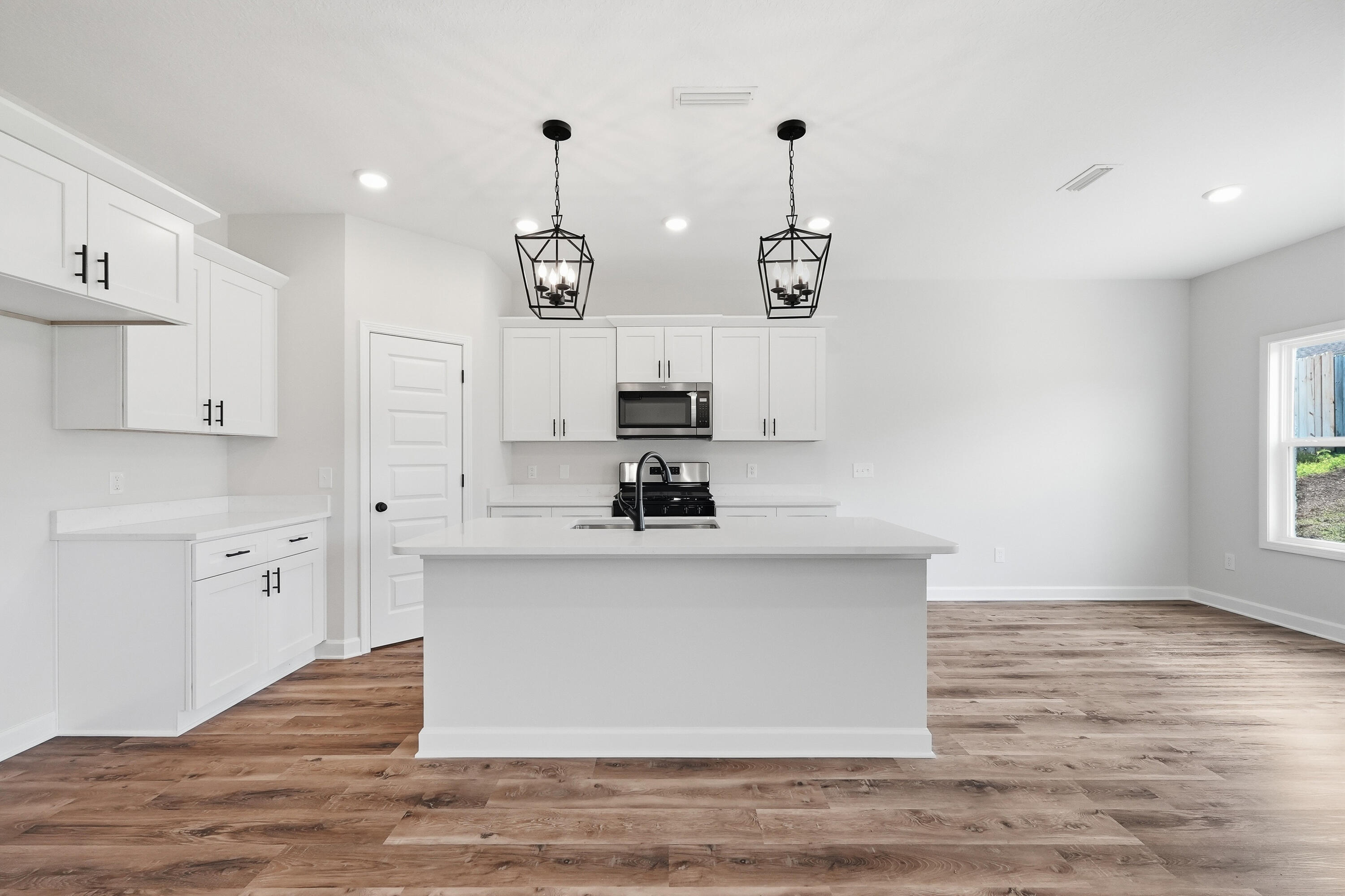 Vacant kitchen with white cabinets, a large island, stainless steel appliances, and wood-look flooring.