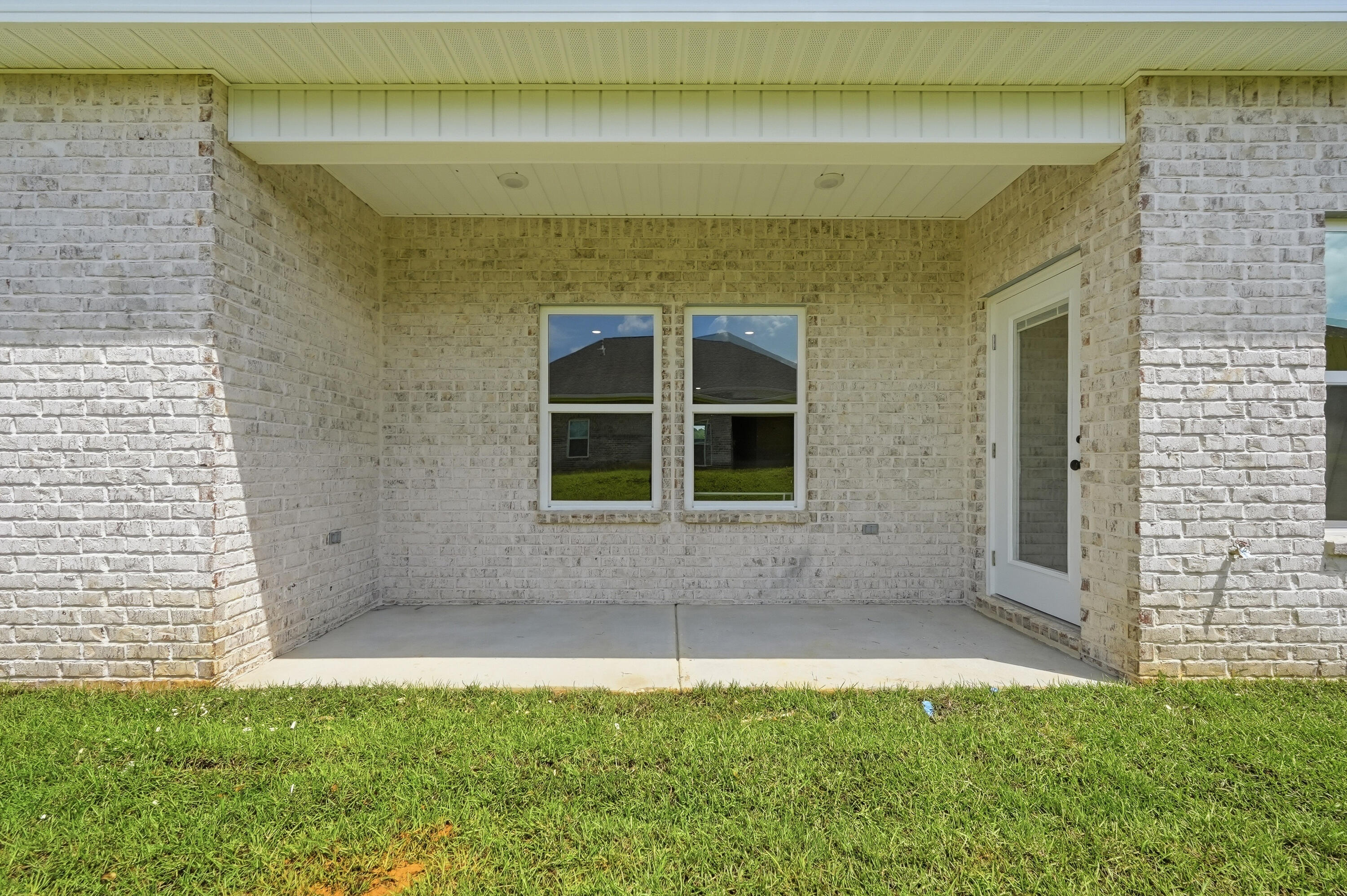 Covered brick patio with two windows and a glass door overlooking a green lawn.