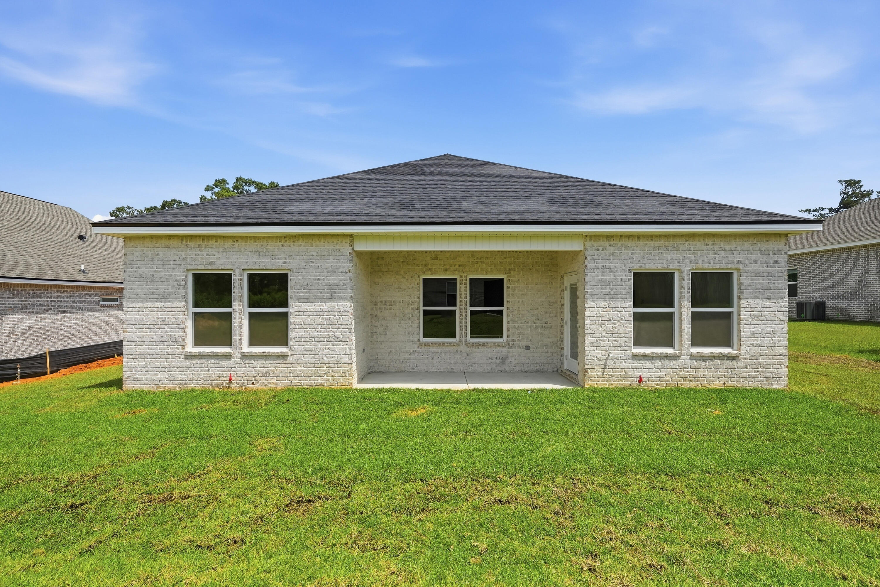 Rear of a light brick house with a covered patio and broad green lawn.
