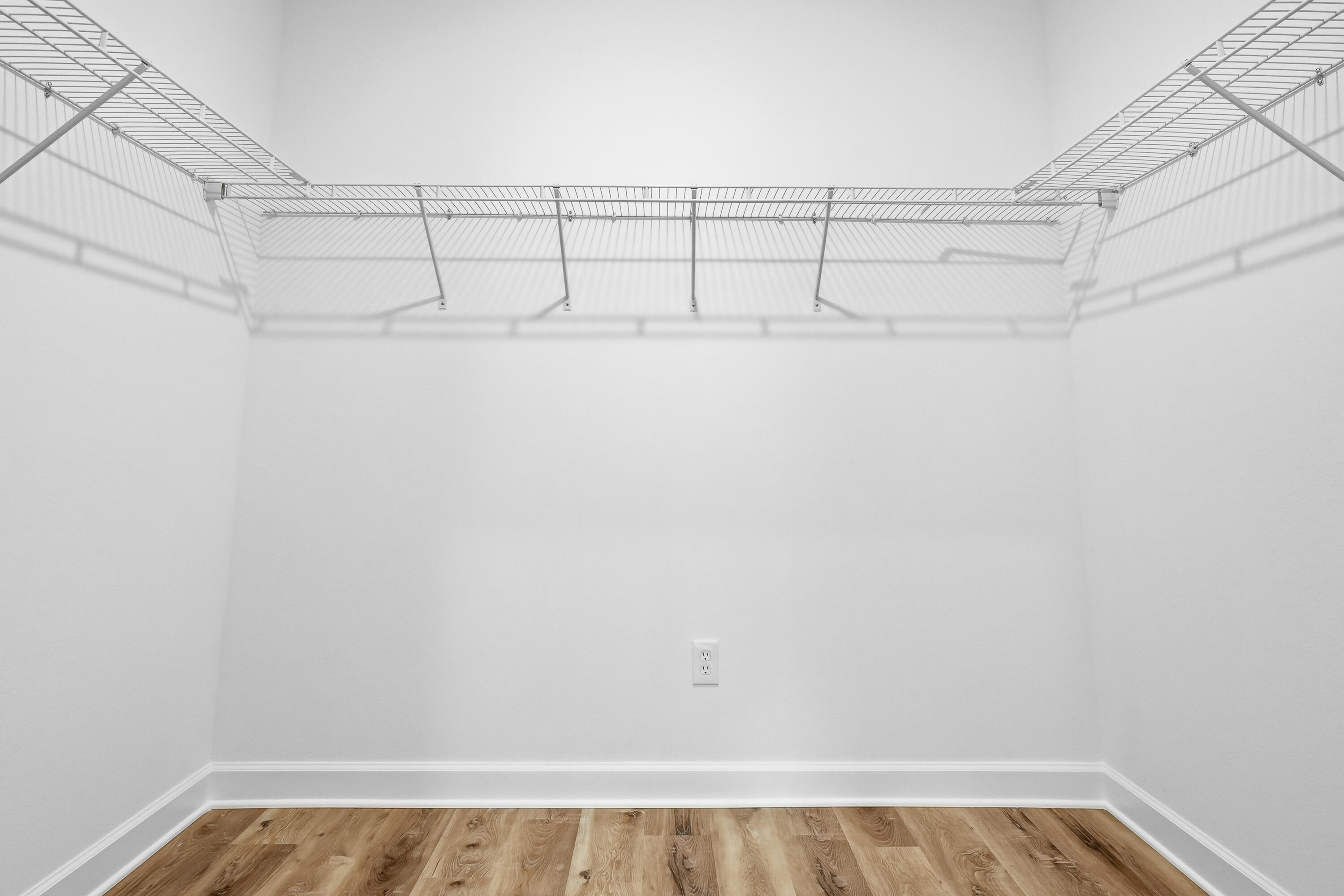 Empty walk-in closet with wraparound wire shelving and wood-look flooring.