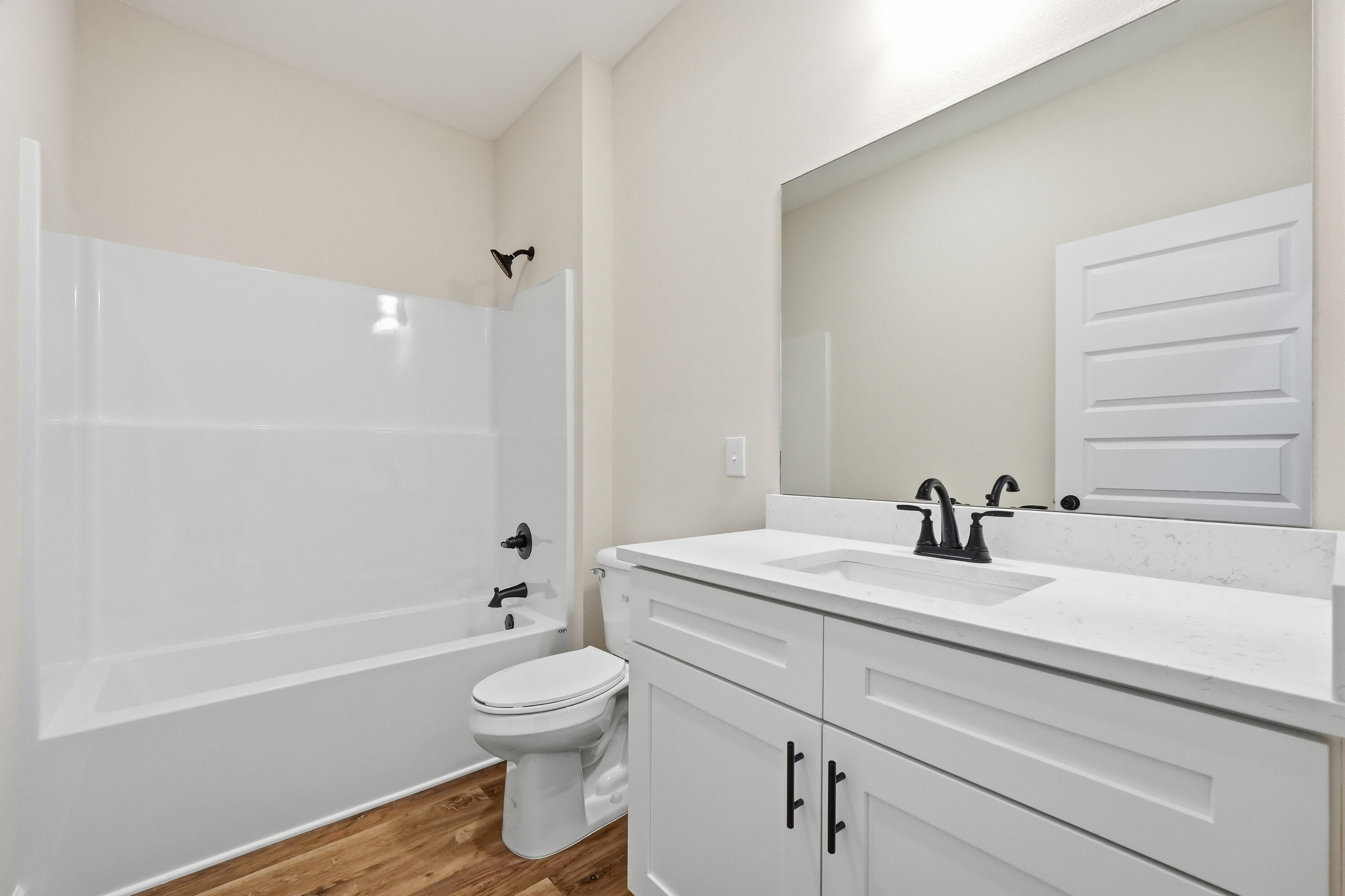 Bathroom with a white tub-shower, stone-counter vanity, black fixtures, and wood-look flooring.