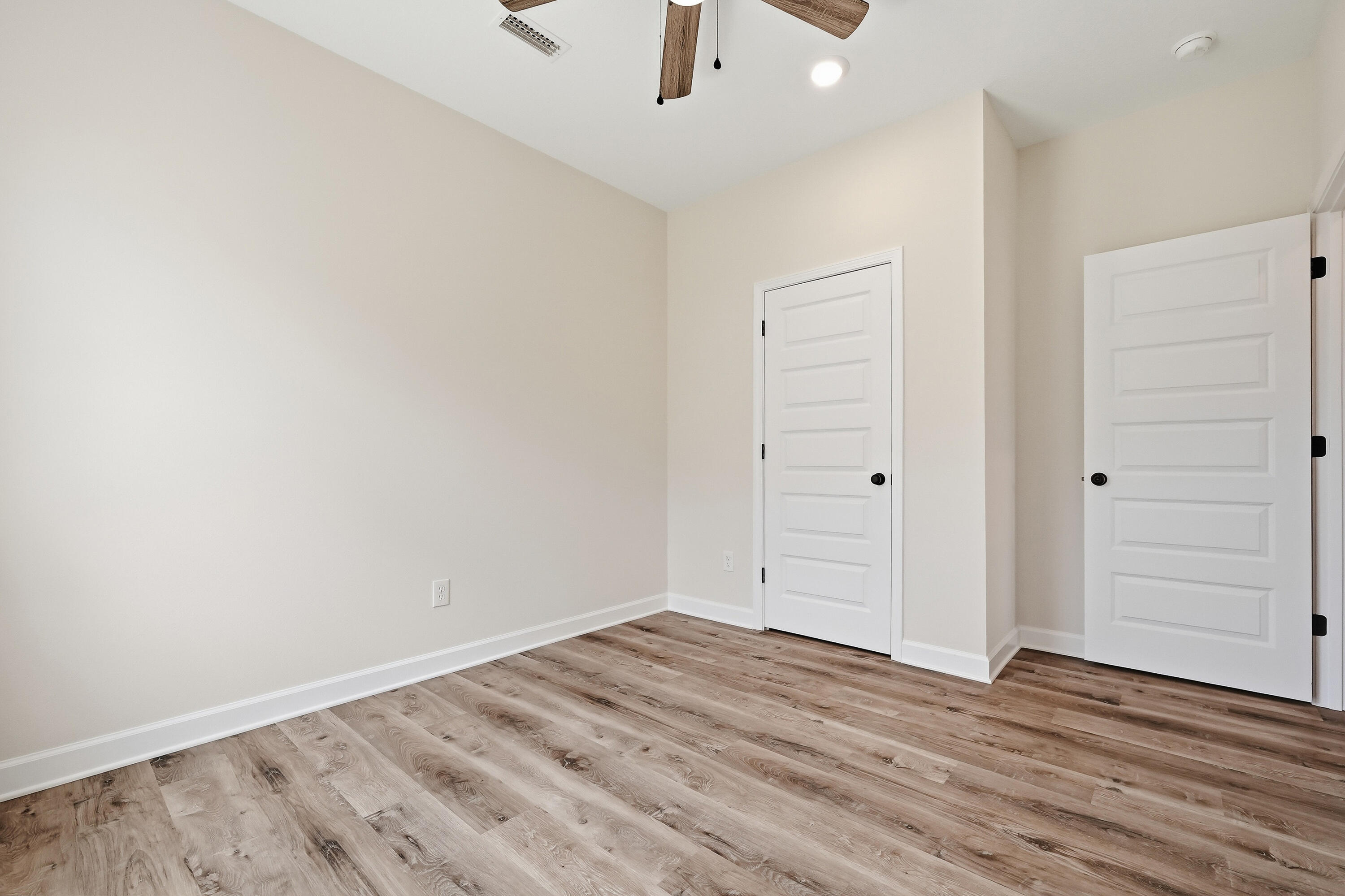 Empty room with wood-look plank flooring, white paneled doors, and a ceiling fan.