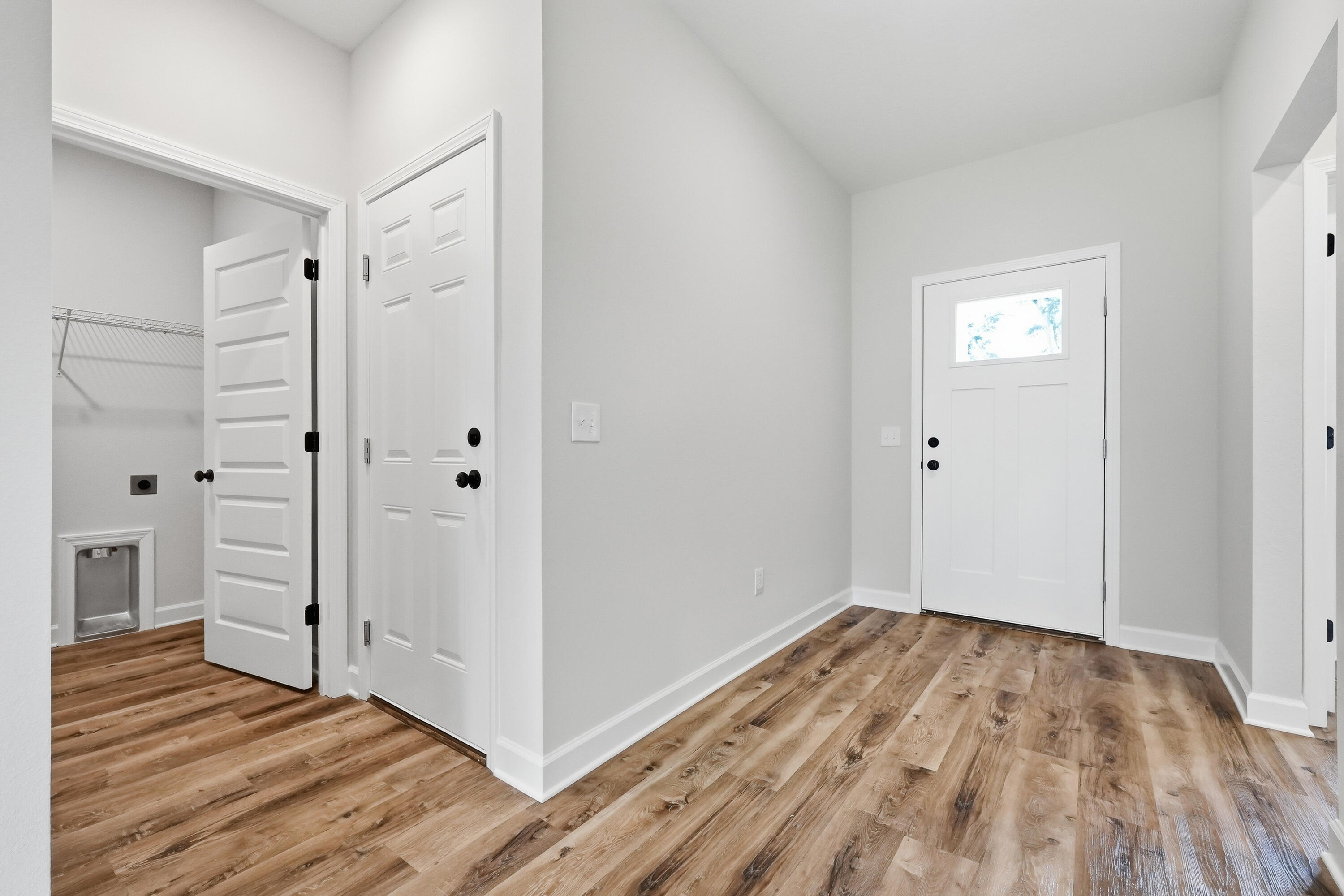Empty entryway with wood-look flooring, a white front door, and an adjacent closet with a pet door.
