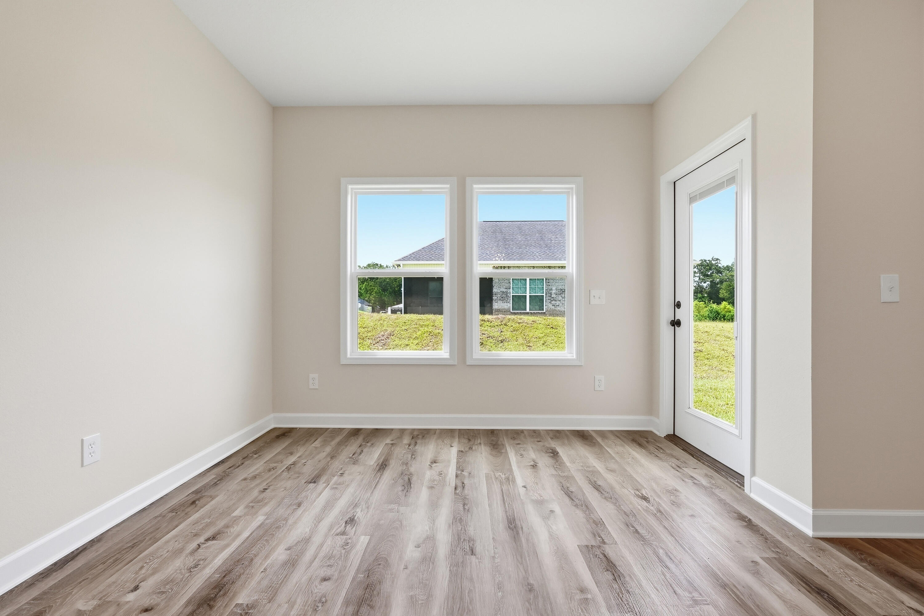 Vacant room with wood-look plank flooring, two windows, and a glass-paneled exterior door.
