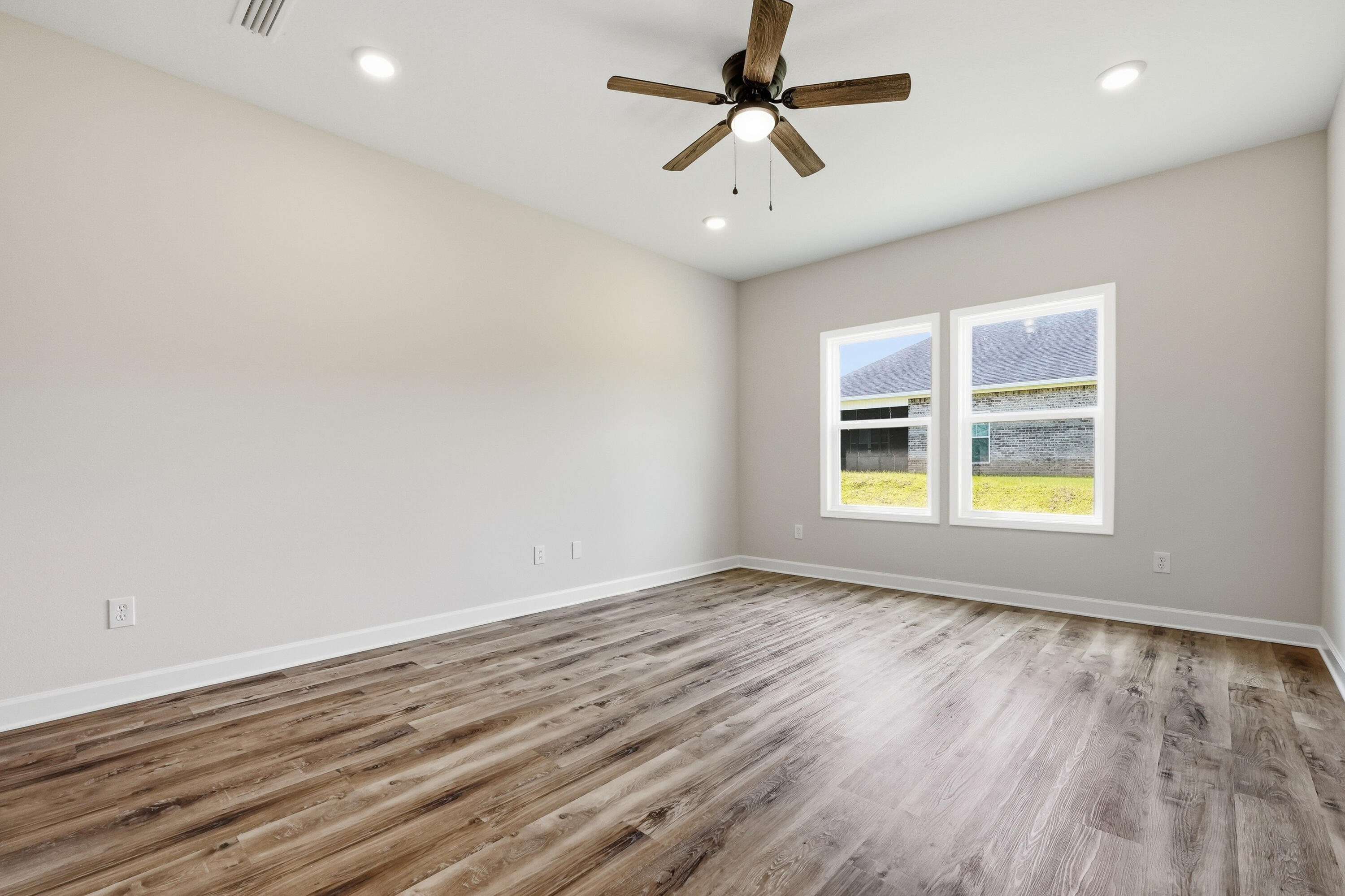 Empty room with wood-look plank flooring, a ceiling fan, and two windows.