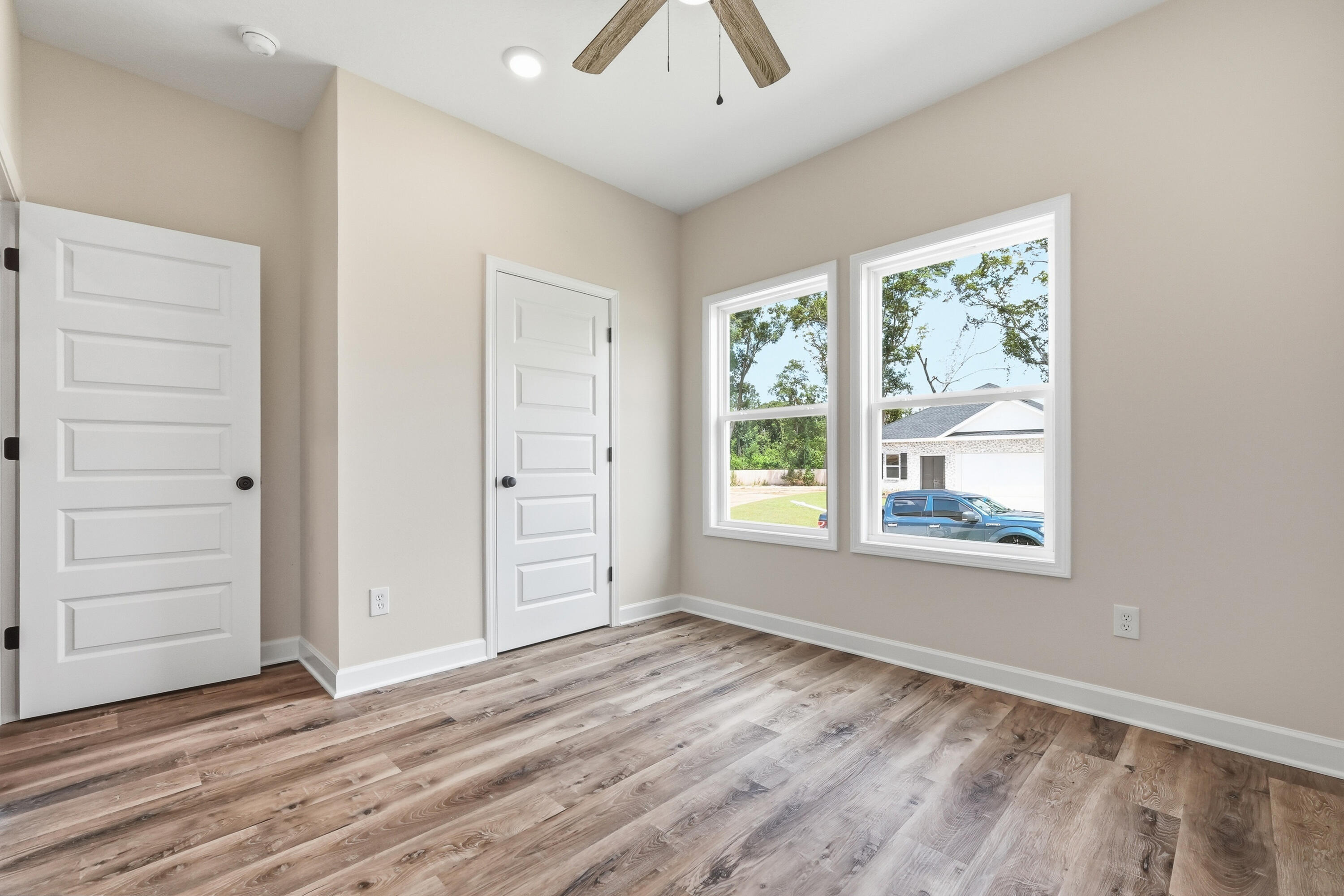 Empty room with wood-look flooring, two windows, and a ceiling fan.