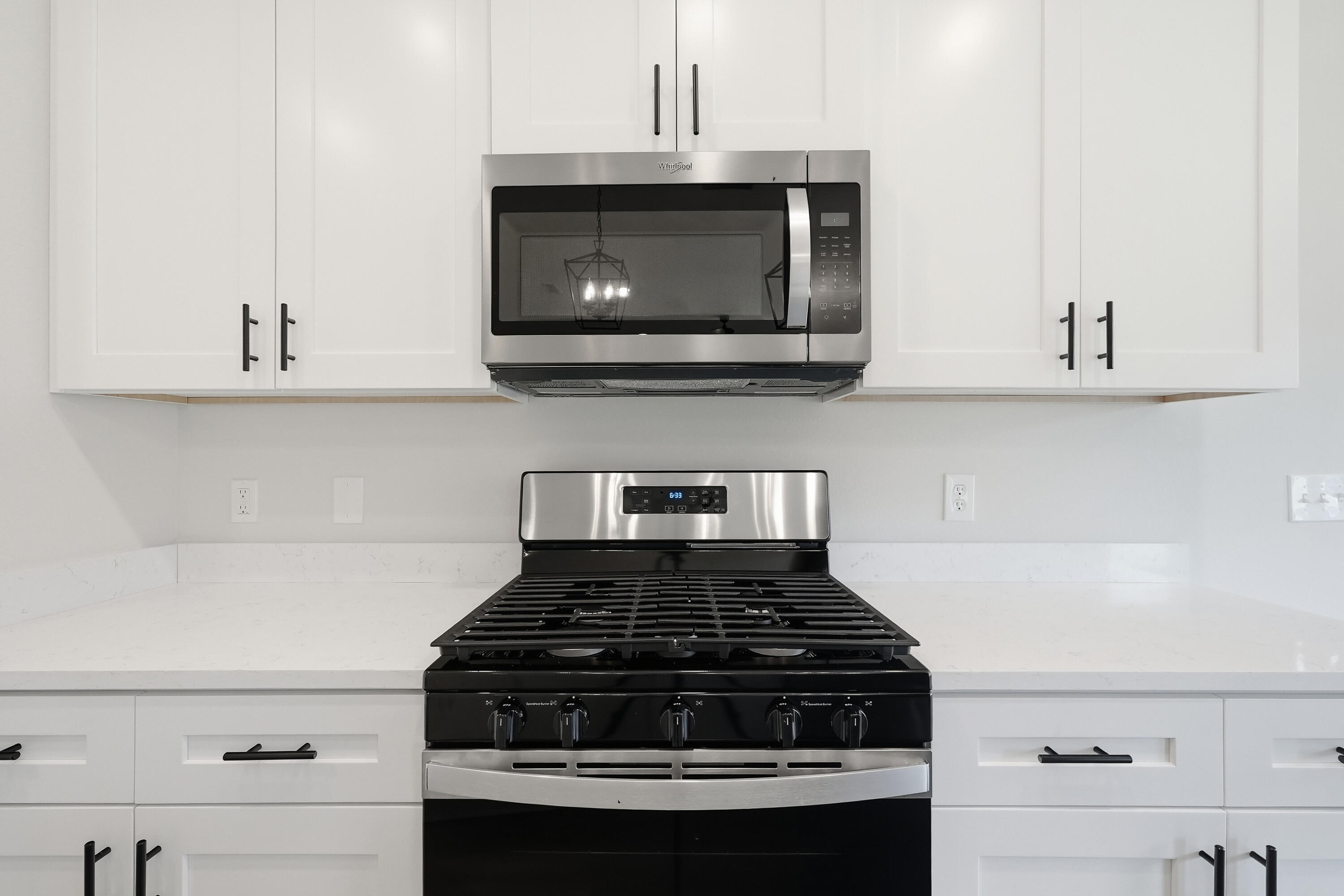 White kitchen with a stainless steel microwave above a black gas range and light countertops.