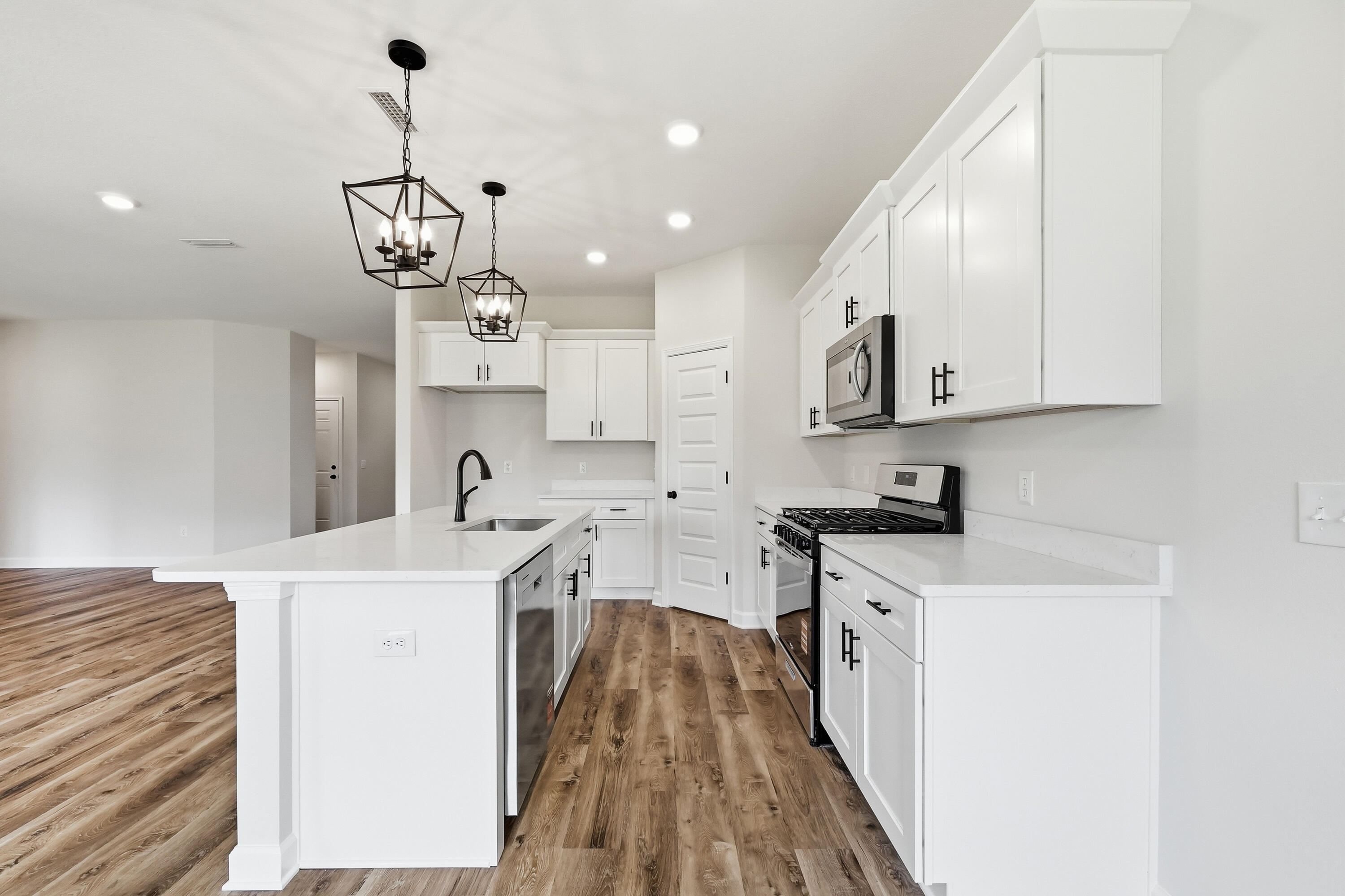 Vacant kitchen with a large white island, shaker cabinets, stainless appliances, and wood-look flooring.