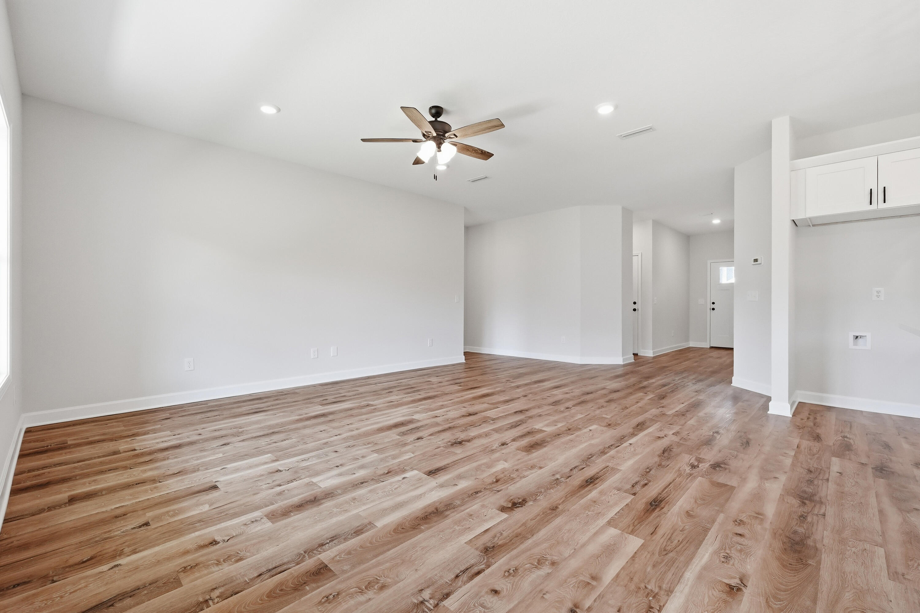Vacant open living area with wood-look plank flooring and a ceiling fan.
