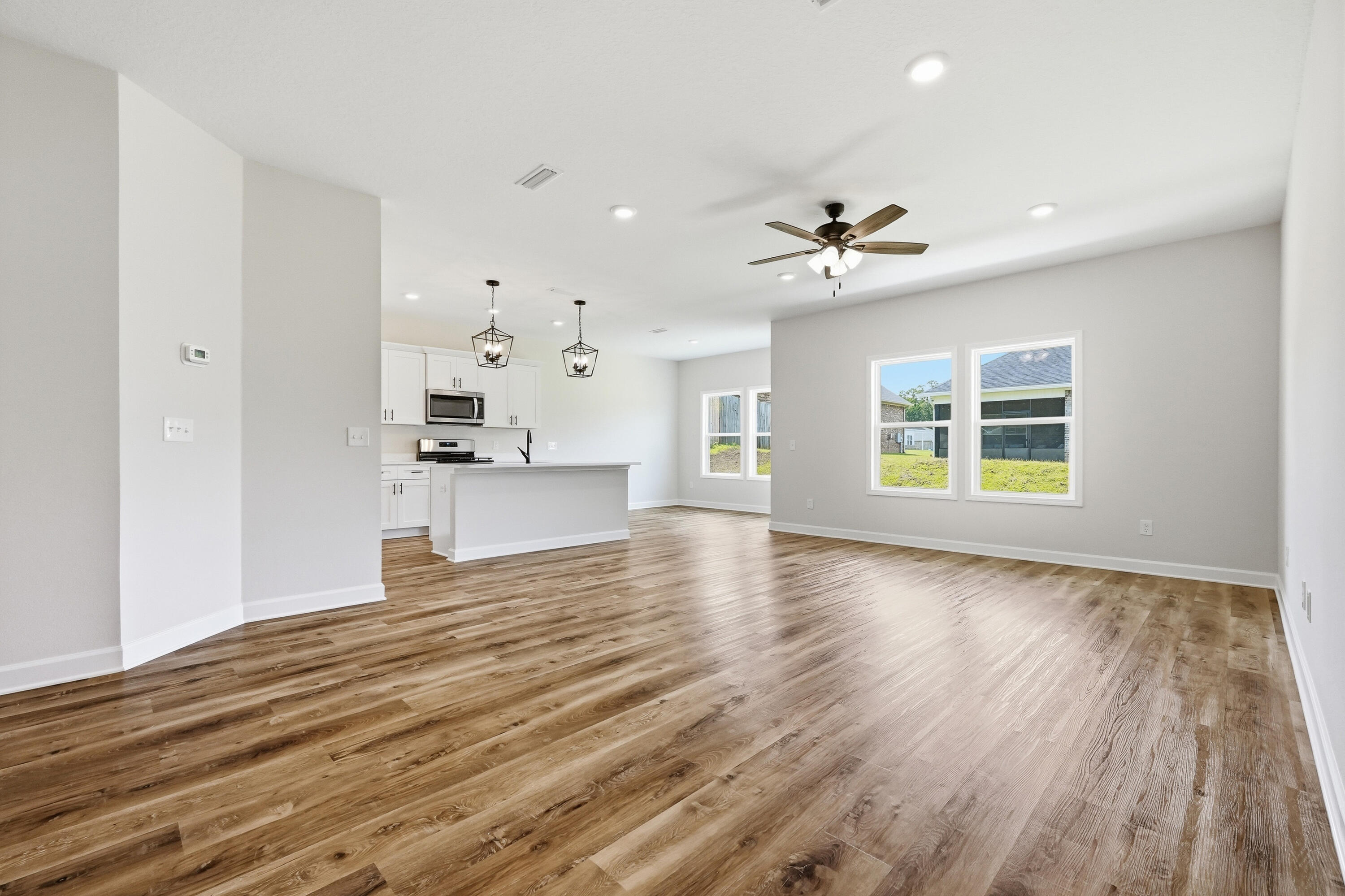 Vacant open-plan living area with wood-look flooring, a kitchen island, and windows overlooking the yard.