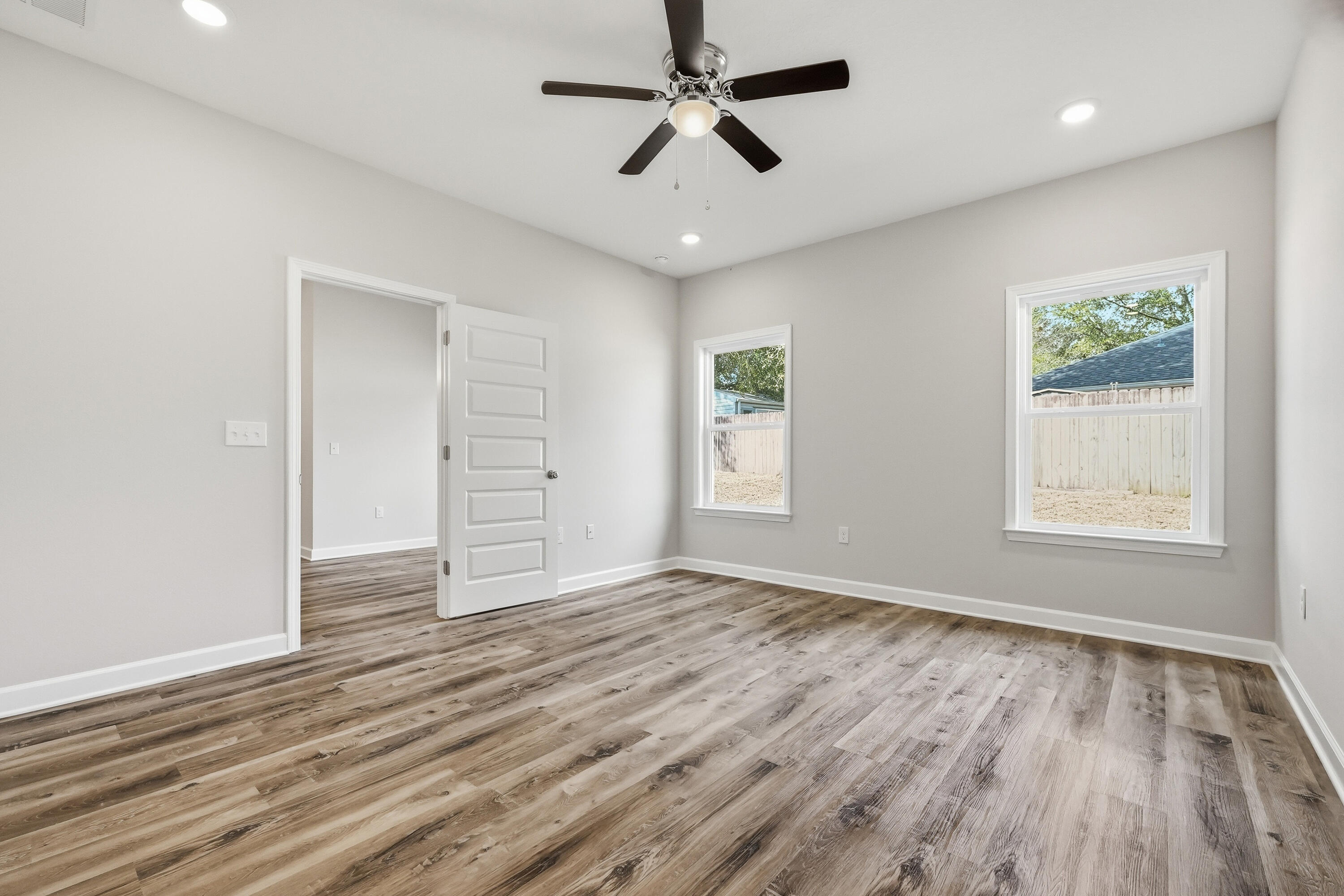 Empty bedroom with wood-look floors, two windows, and a ceiling fan.