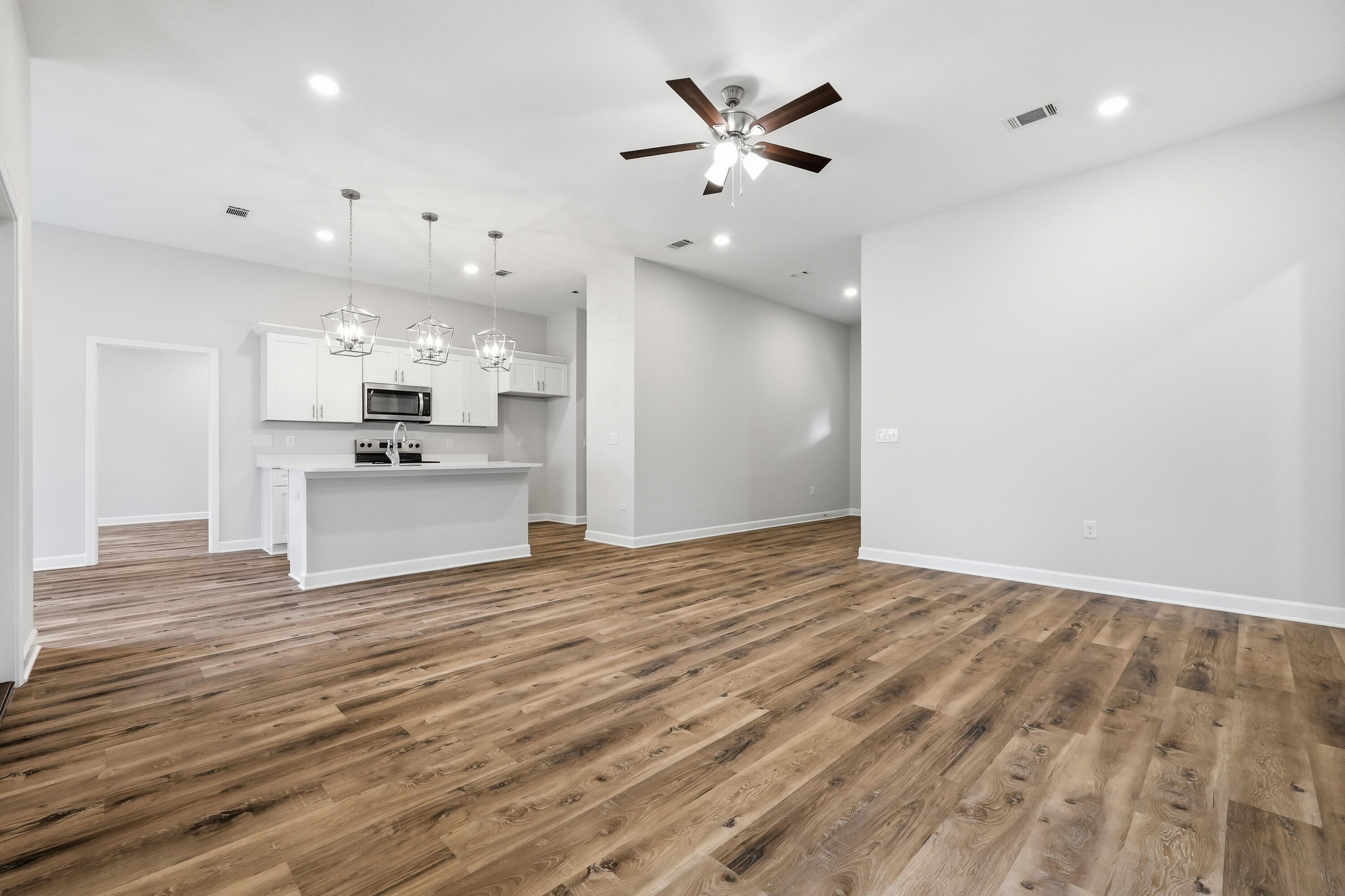 Vacant open-plan kitchen with white cabinets, a peninsula, and wood-look plank flooring.