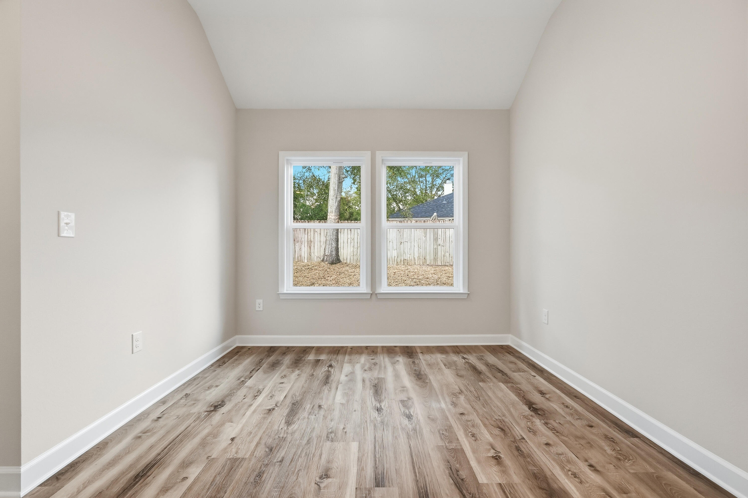 Empty room with wood-look plank flooring and two windows overlooking a fenced yard.