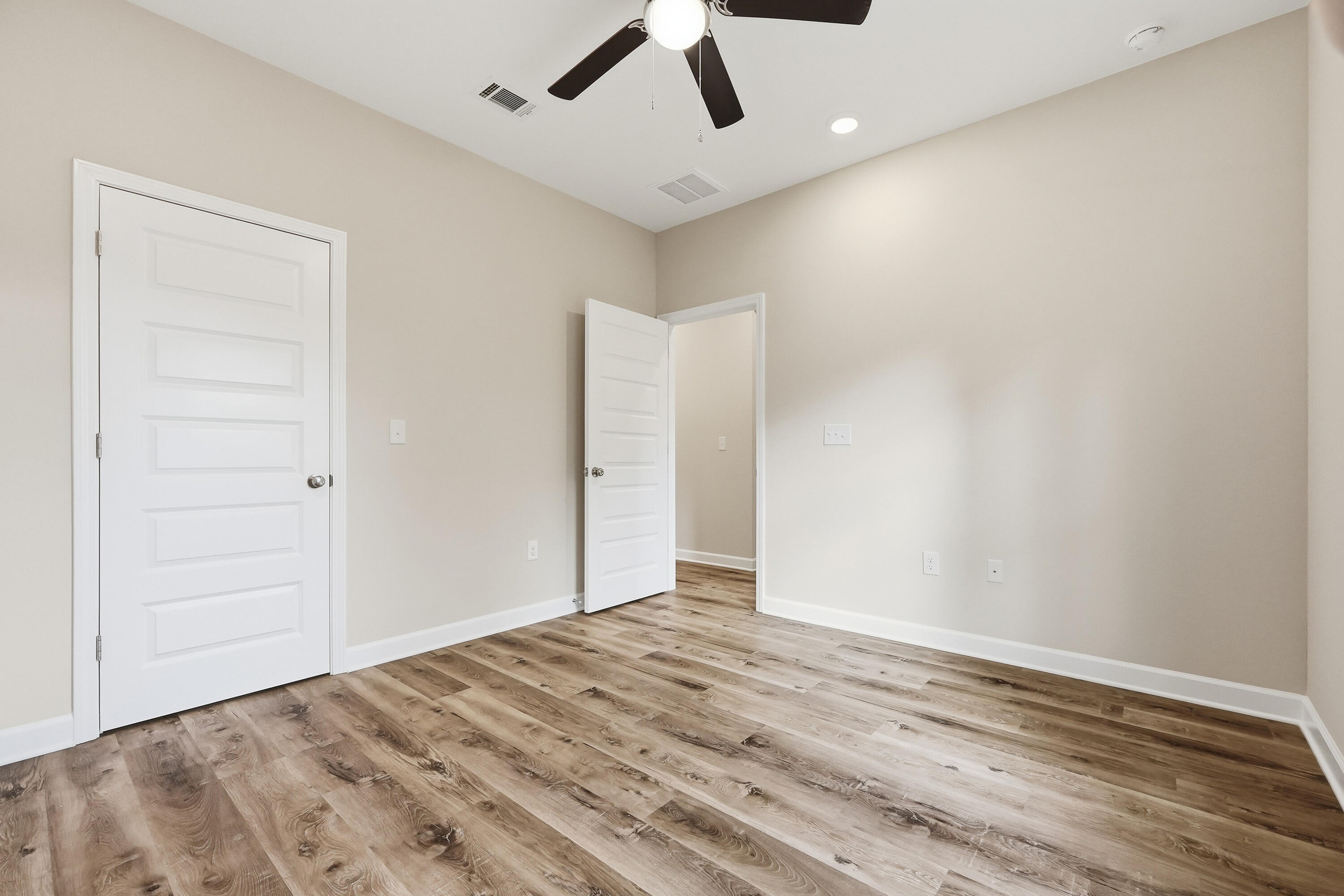 Empty room with wood-look flooring, two white doors, and a ceiling fan.