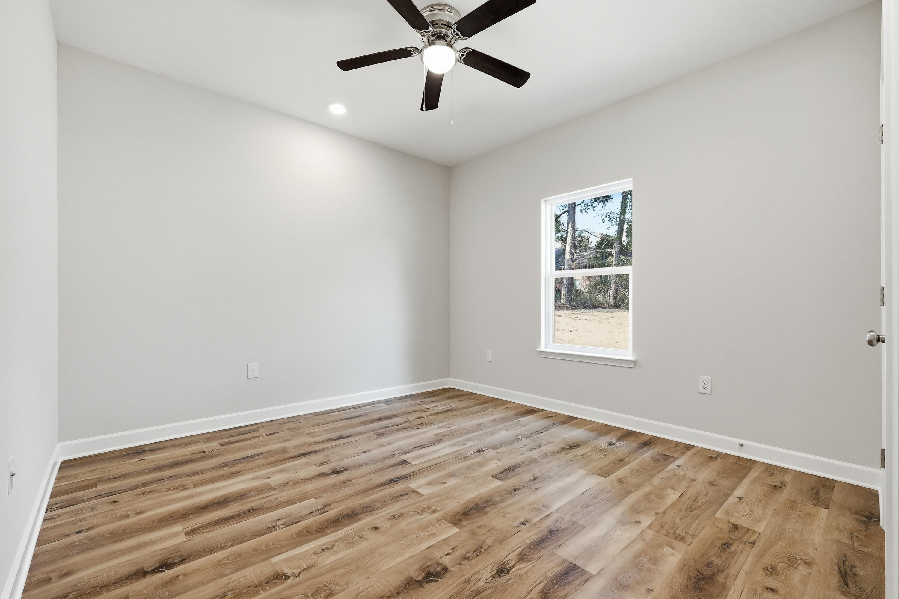 Empty room with wood-look plank floors, a single window, and a ceiling fan.